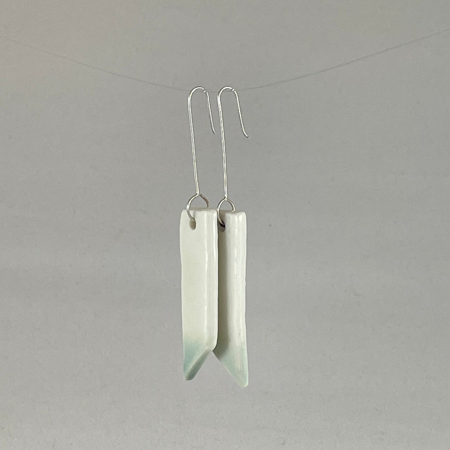 A pair of hand formed porcelain pendant earrings in glossy white and a hint of mint green. Side view showing thin earring profile