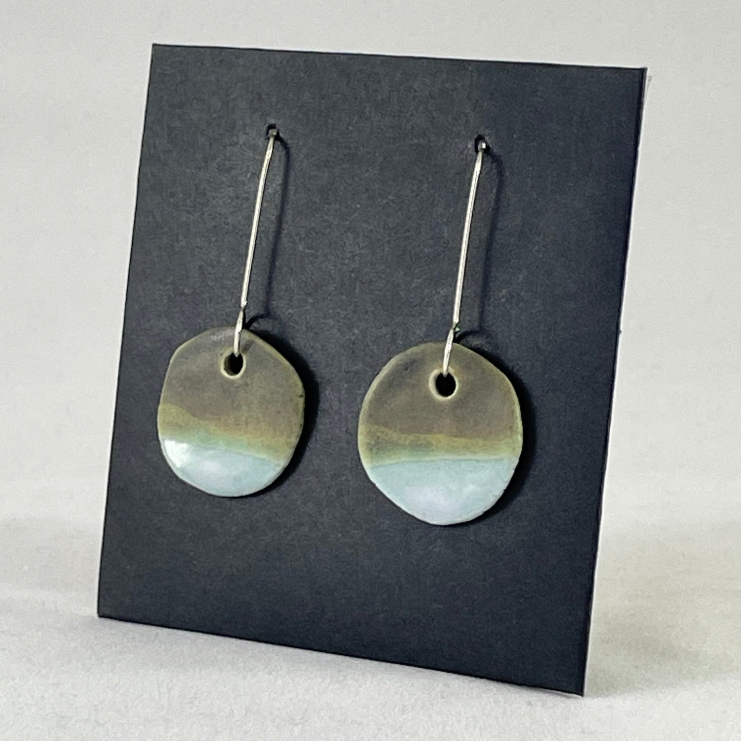 A pair of circular porcelain earrings in blue and green. On sterling silver earrings hooks. Side view