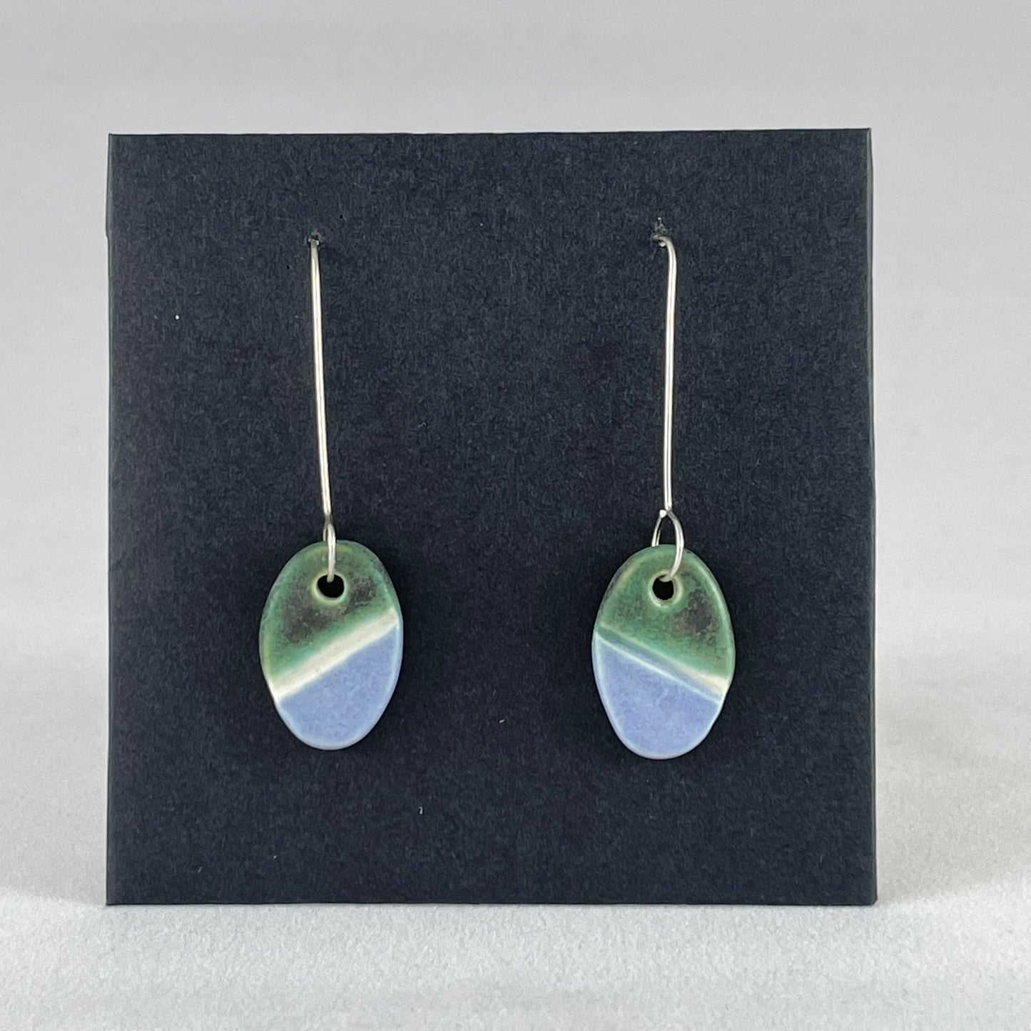 A pair of green, white and lilac-blue earrings on a black background.