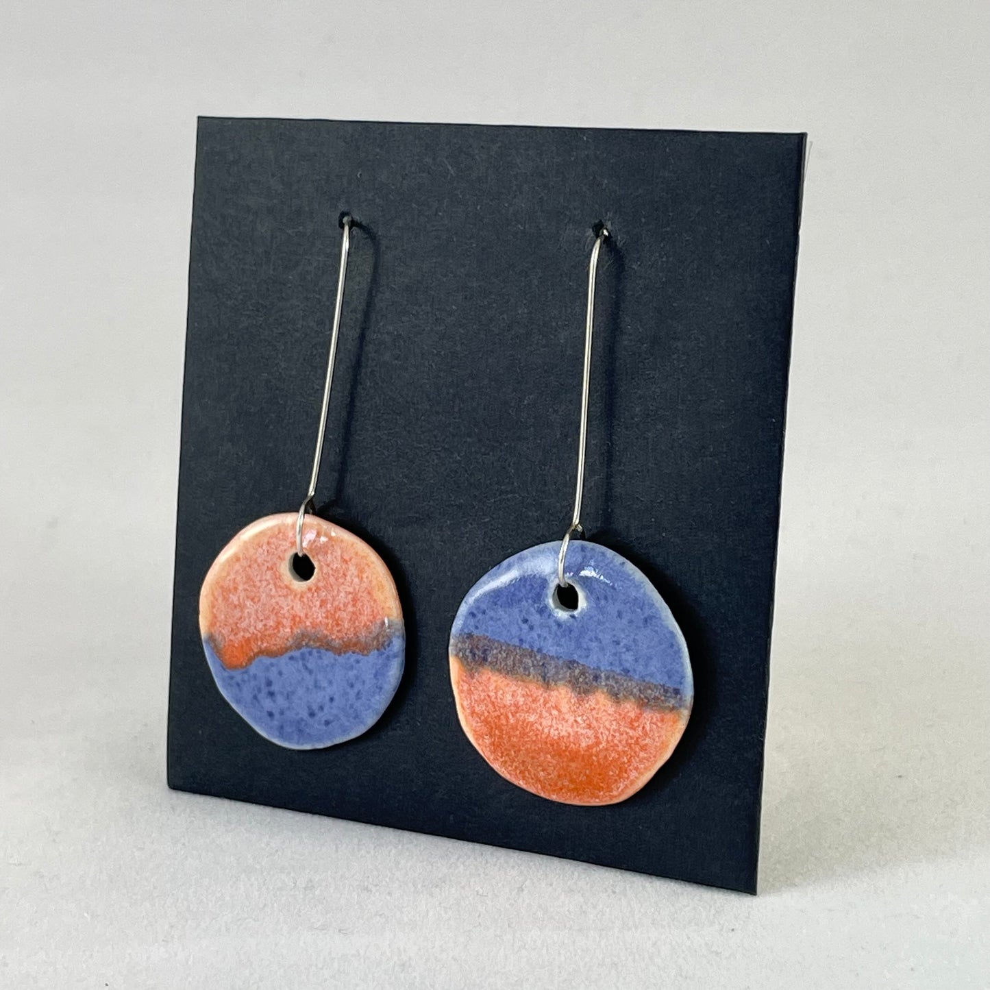 A pair of circular shaped porcelain earrings in blue and orange. On sterling silver earrings hooks. side view