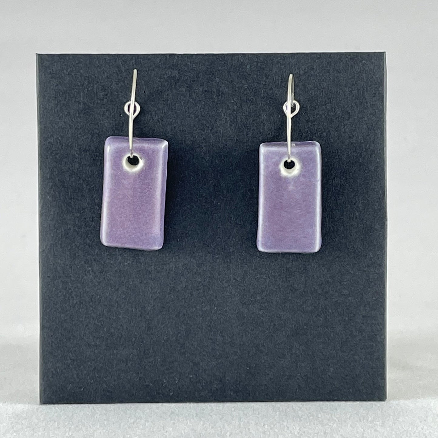 A pair of rectangular shaped porcelain hoop earrings in purple. On sterling silver earrings hooks.