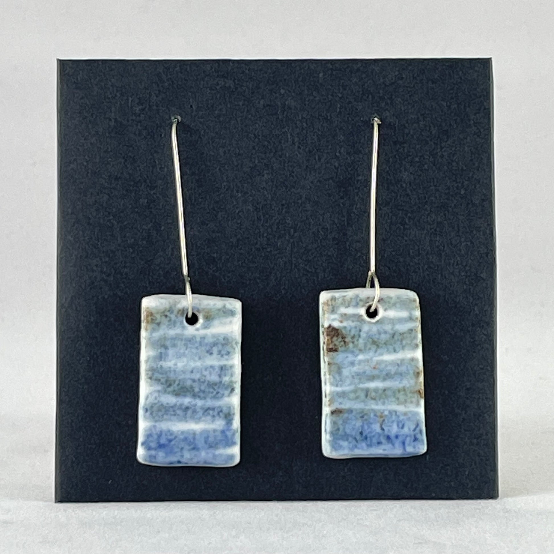 A pair of blue green and white porcelain earrings. Photographed on a black background. On sterling silver earrings hooks.
