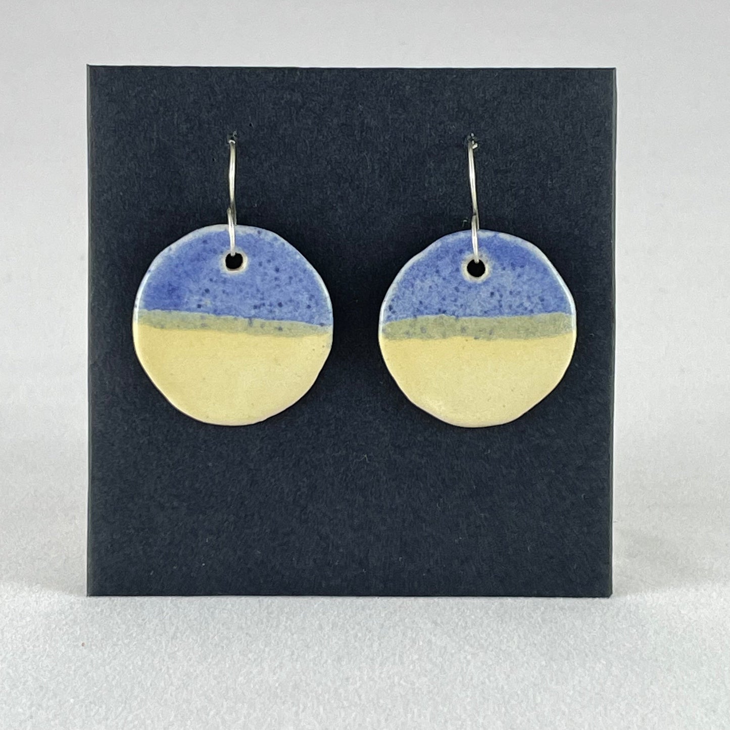 A pair of circular porcelain earrings in yellow and blue. On sterling silver earrings hooks.