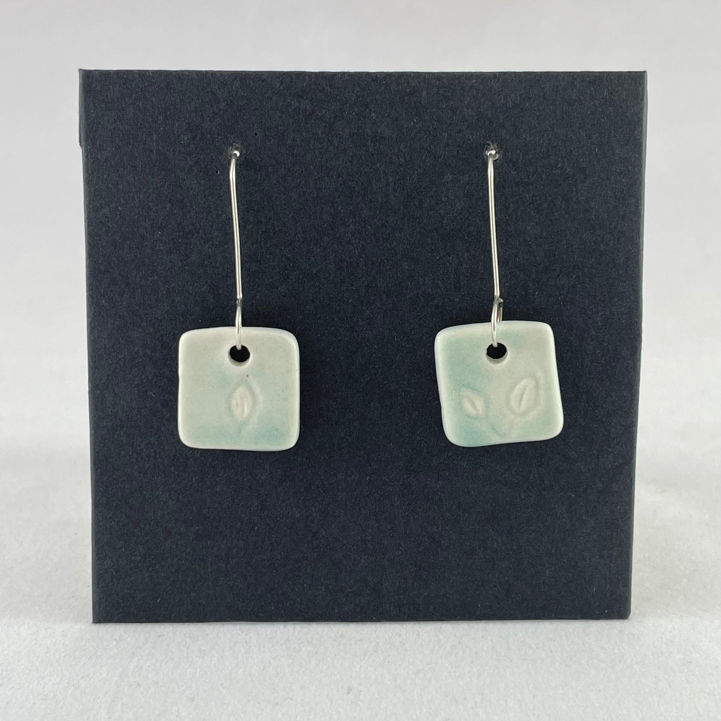 A pair of mint green square porcelain earrings on a black background. On sterling silver earrings hooks.