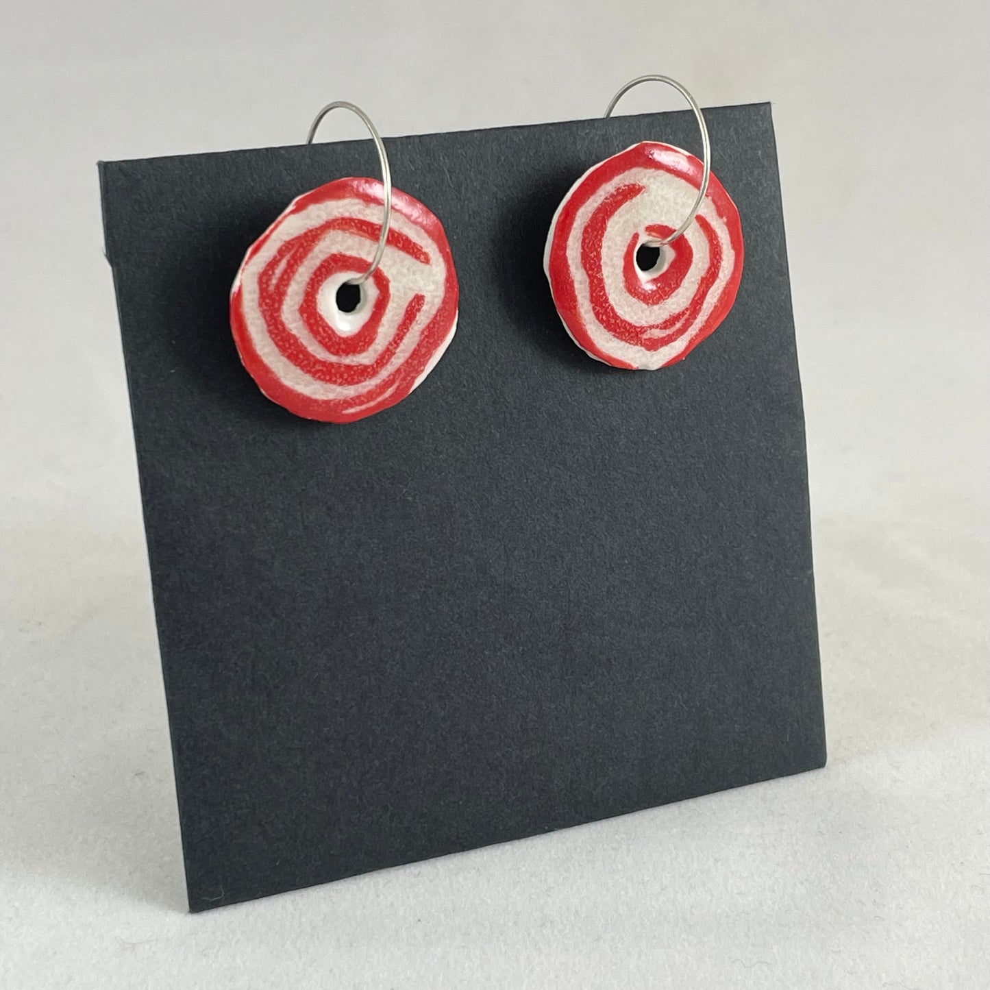 A pair of red and white porcelain earrings on a black background. Simple rose pattern. Side view.