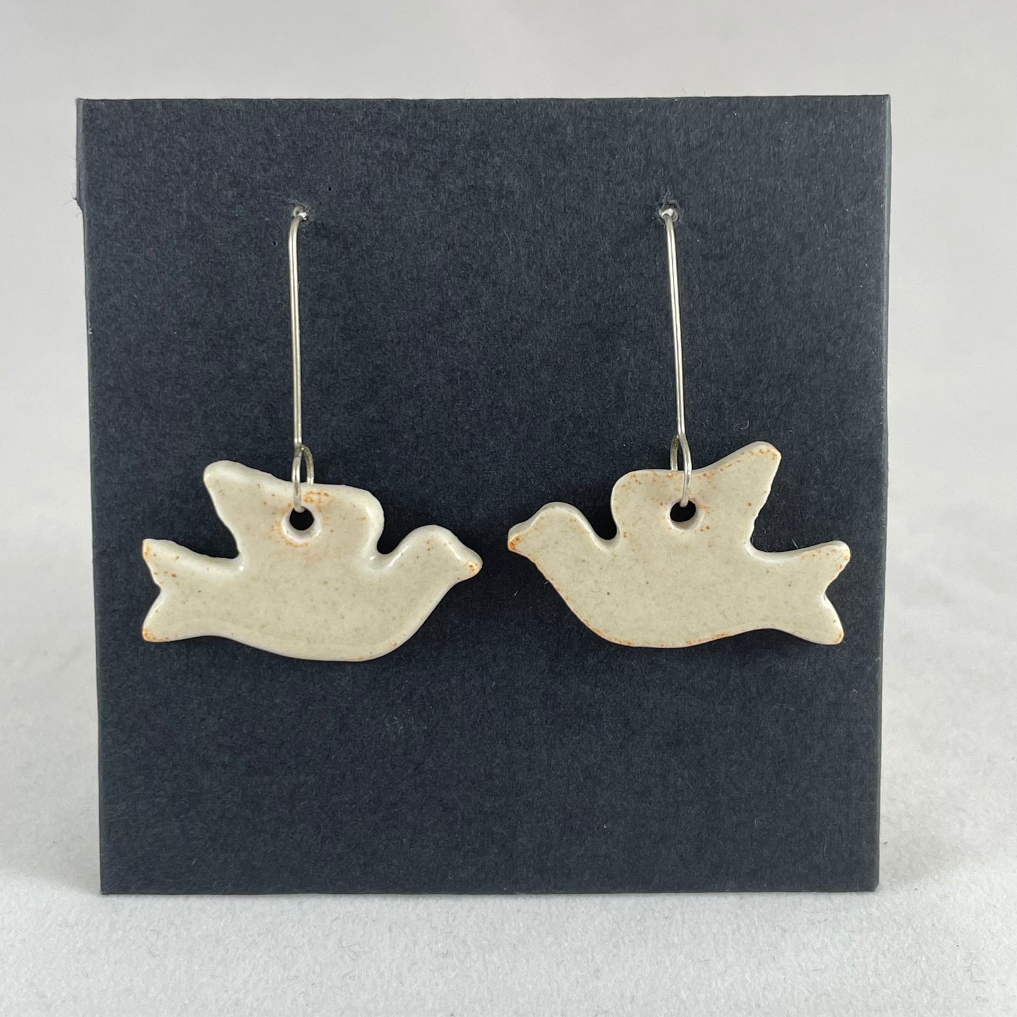A pair of cream porcelain earrings in the shape of flying dove on a black background.