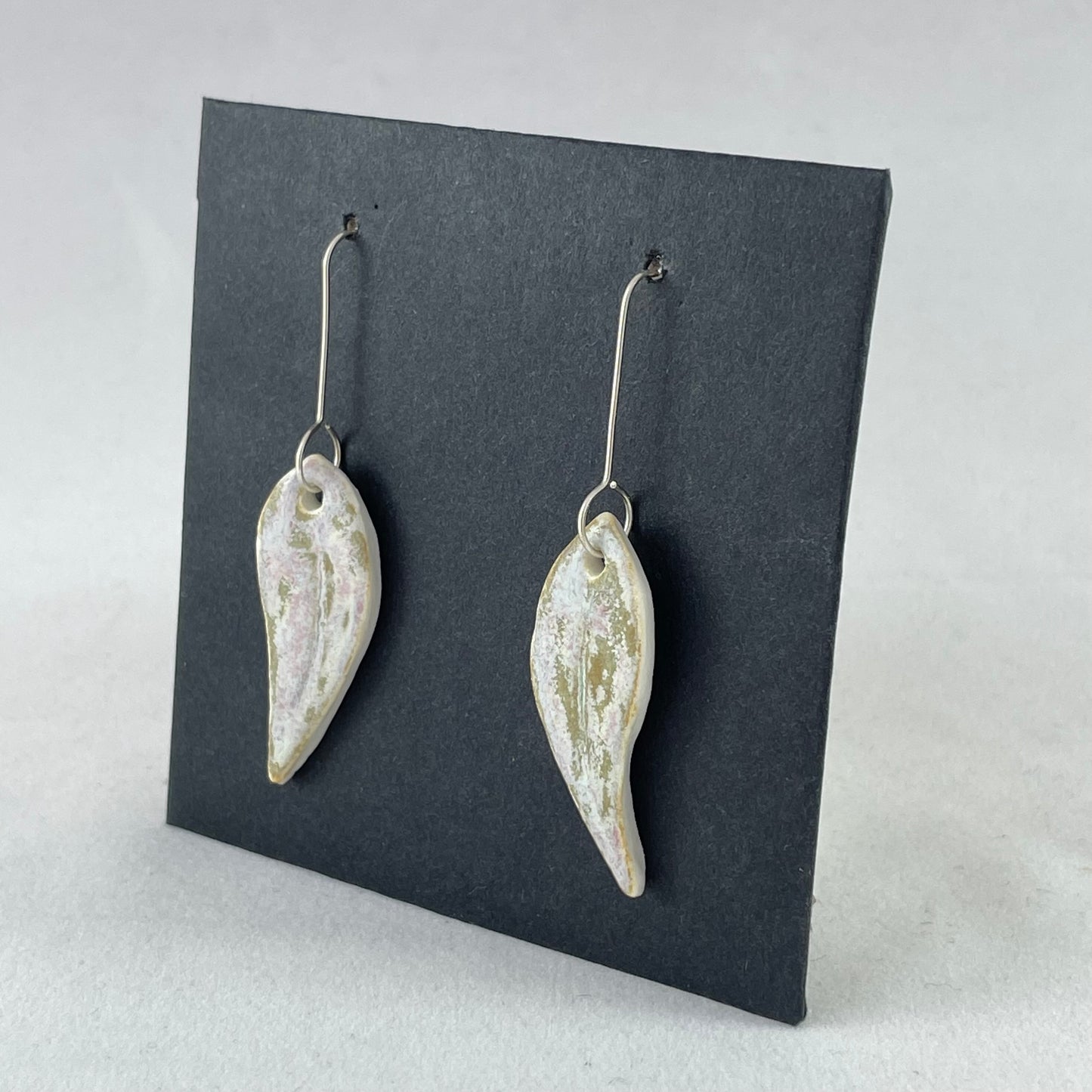 A pair of porcelain earrings in organic gum leaf shape. Photographed on a black background. Side view facing left