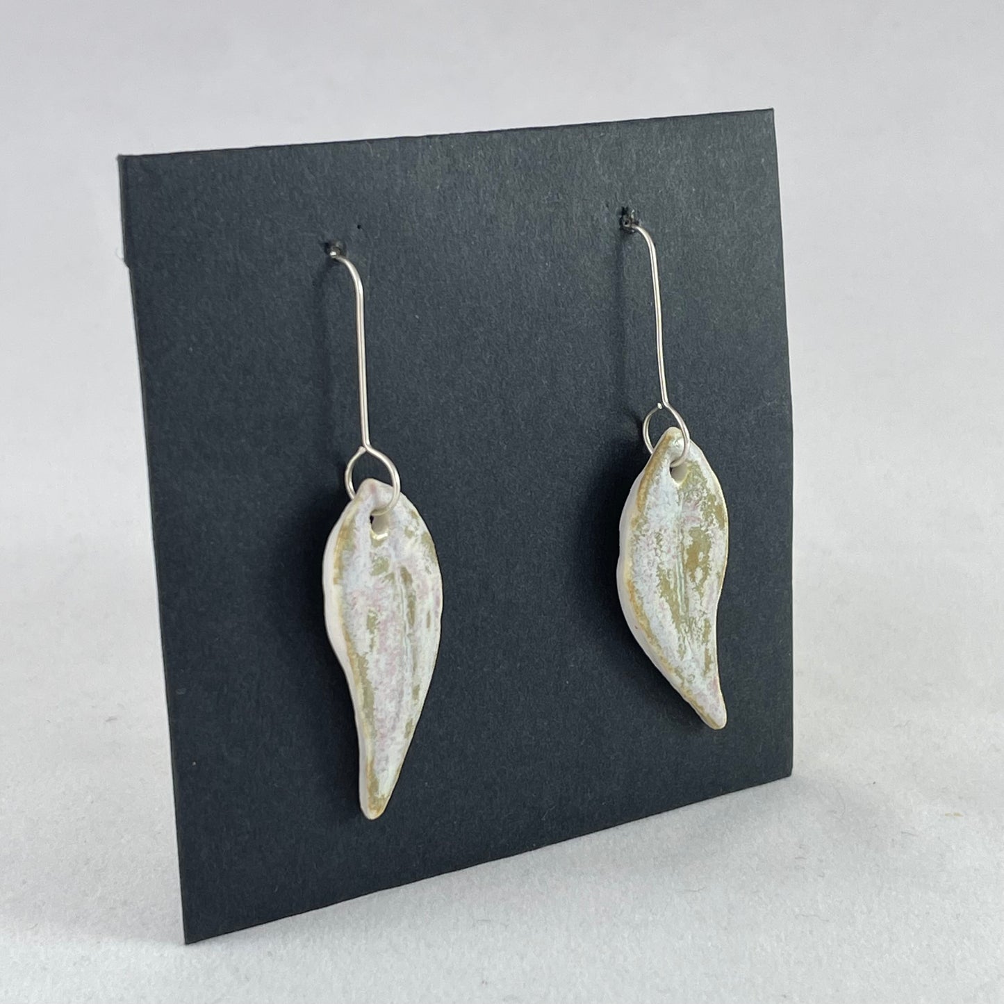 A pair of porcelain earrings in organic gum leaf shape. Photographed on a black background. Side view facing right