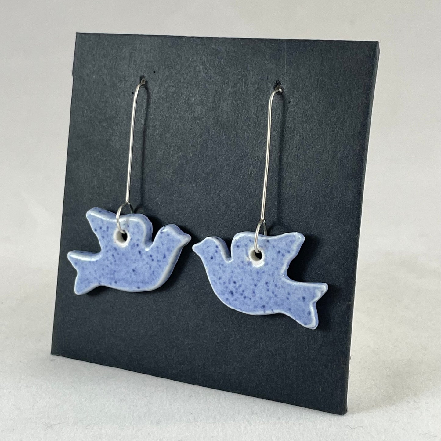 A pair of blue porcelain earrings in the shape of flying dove on a black background. Side view