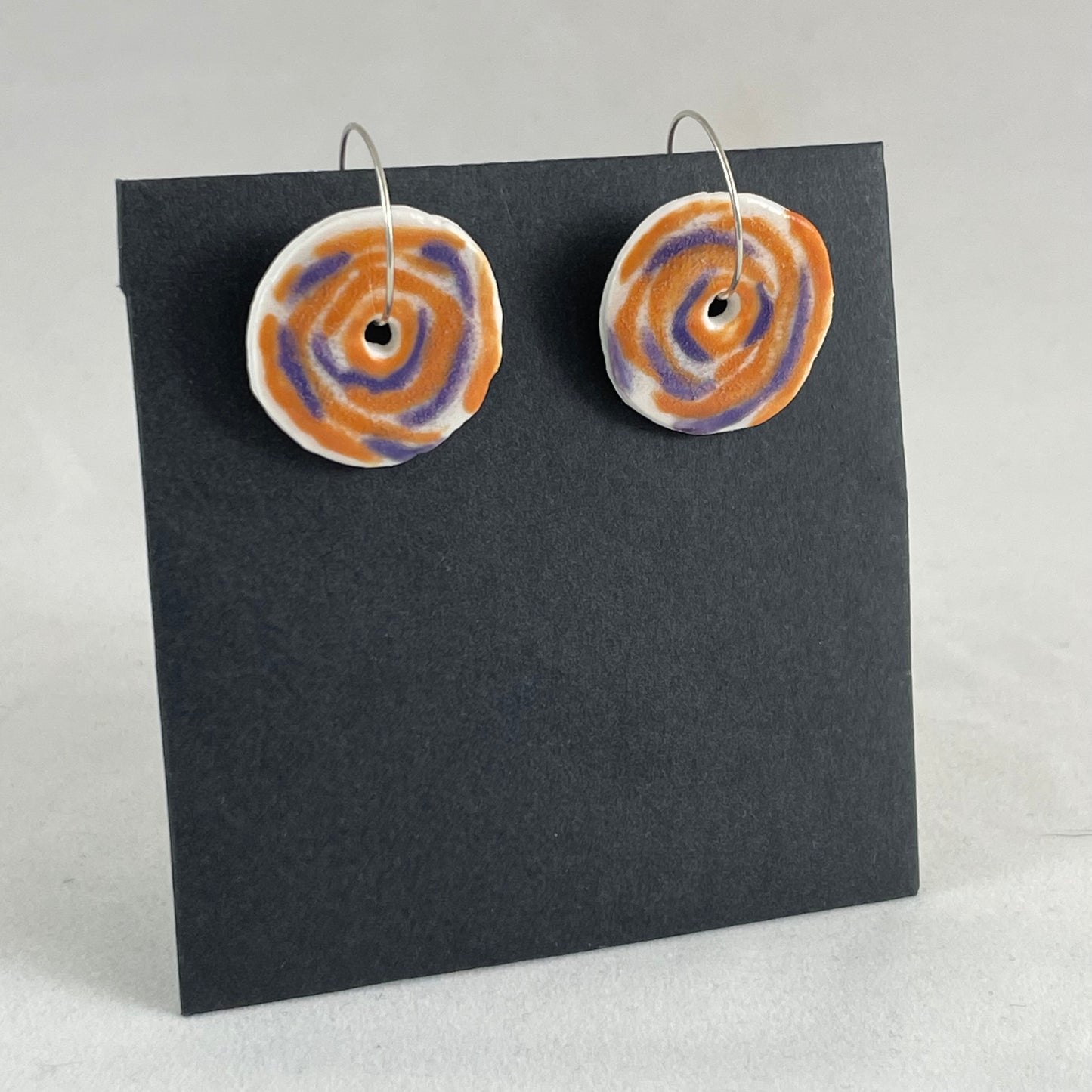 A pair of lavender and orange porcelain earrings on a black background. Simple rose pattern. Side view.