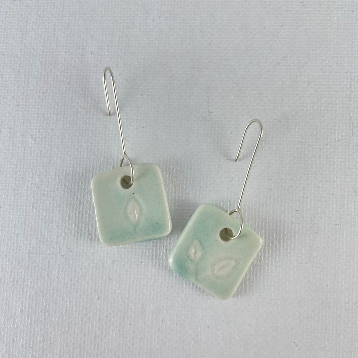 A pair of mint green square porcelain earrings on a white background. On sterling silver earrings hooks.
