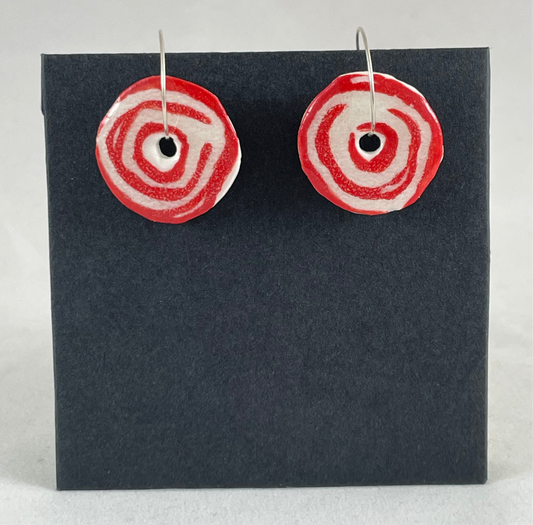 A pair of red and white porcelain earrings hanging on black card. Simple rose pattern with loosely painted red circles on white porcelain.