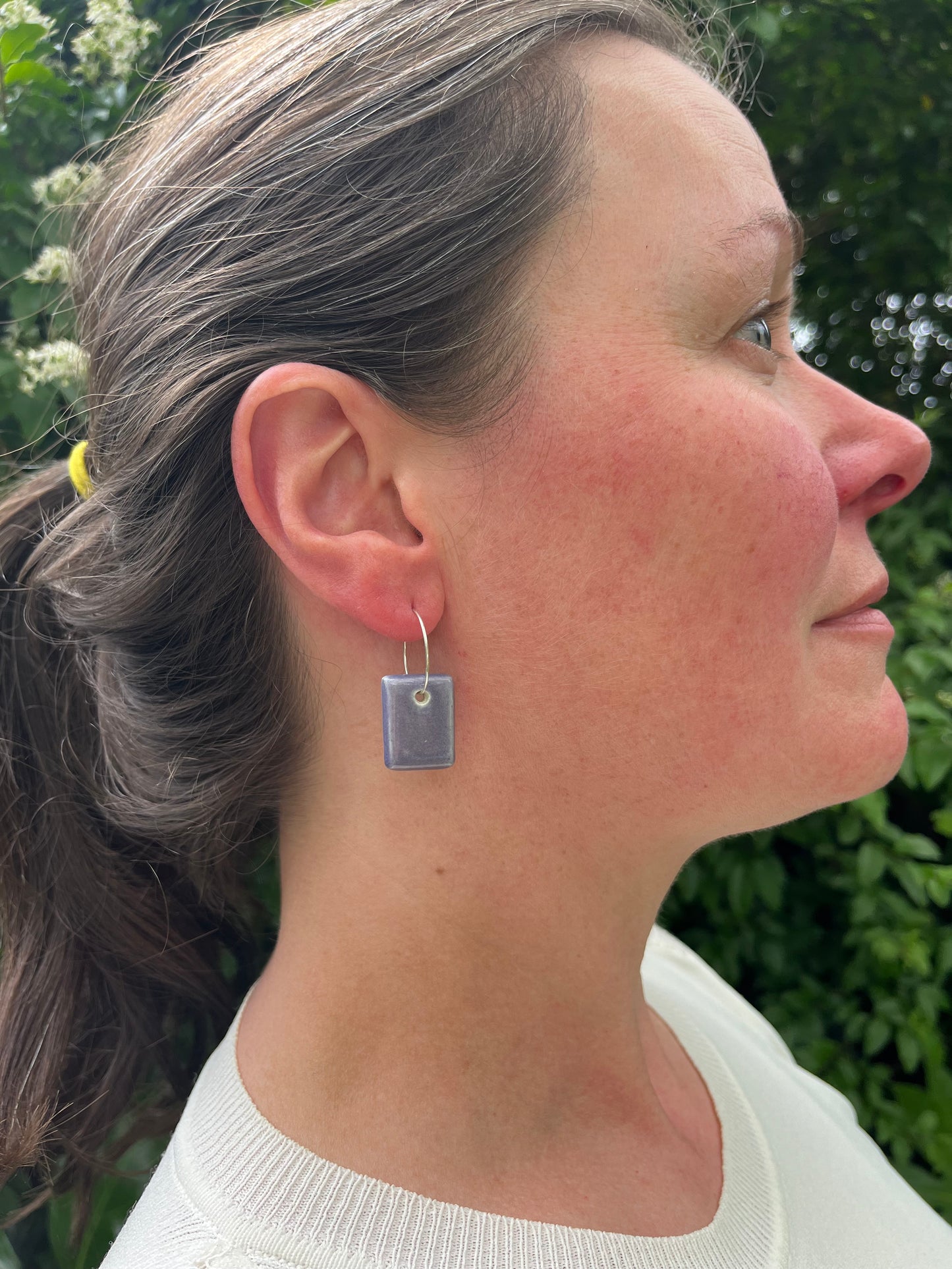 White woman wearing purple pendant earrings looking away from camera. One earring visible. Daylight