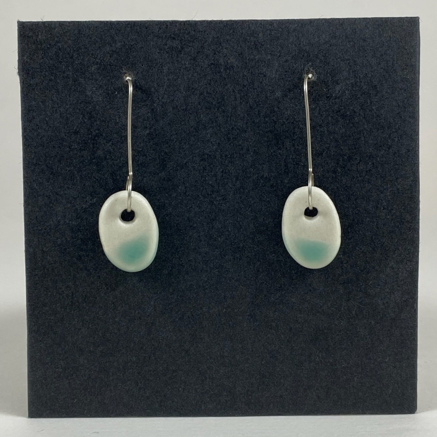 Fine silver hooks with oval shaped pendants in white porcelain. Bottom half dipped in mint green shiny glaze, which fades to white at the edges for a soft look. Photographed on a black background.