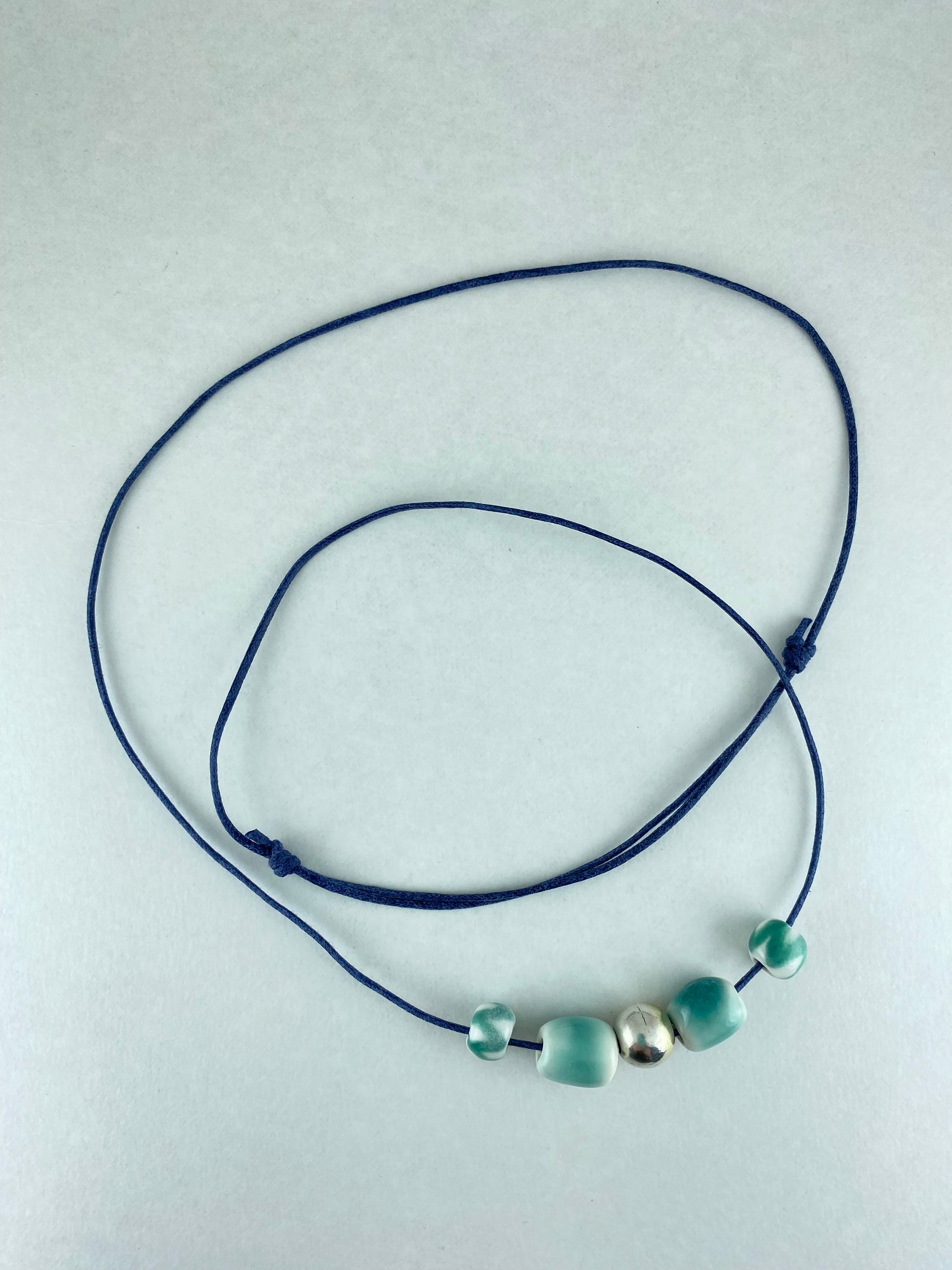 Two small round turquoise beads, two medium sized turquoise beads and a shiny silver bead in the middle. Threaded on thin navy blue cord and photographed laid out on a white background.