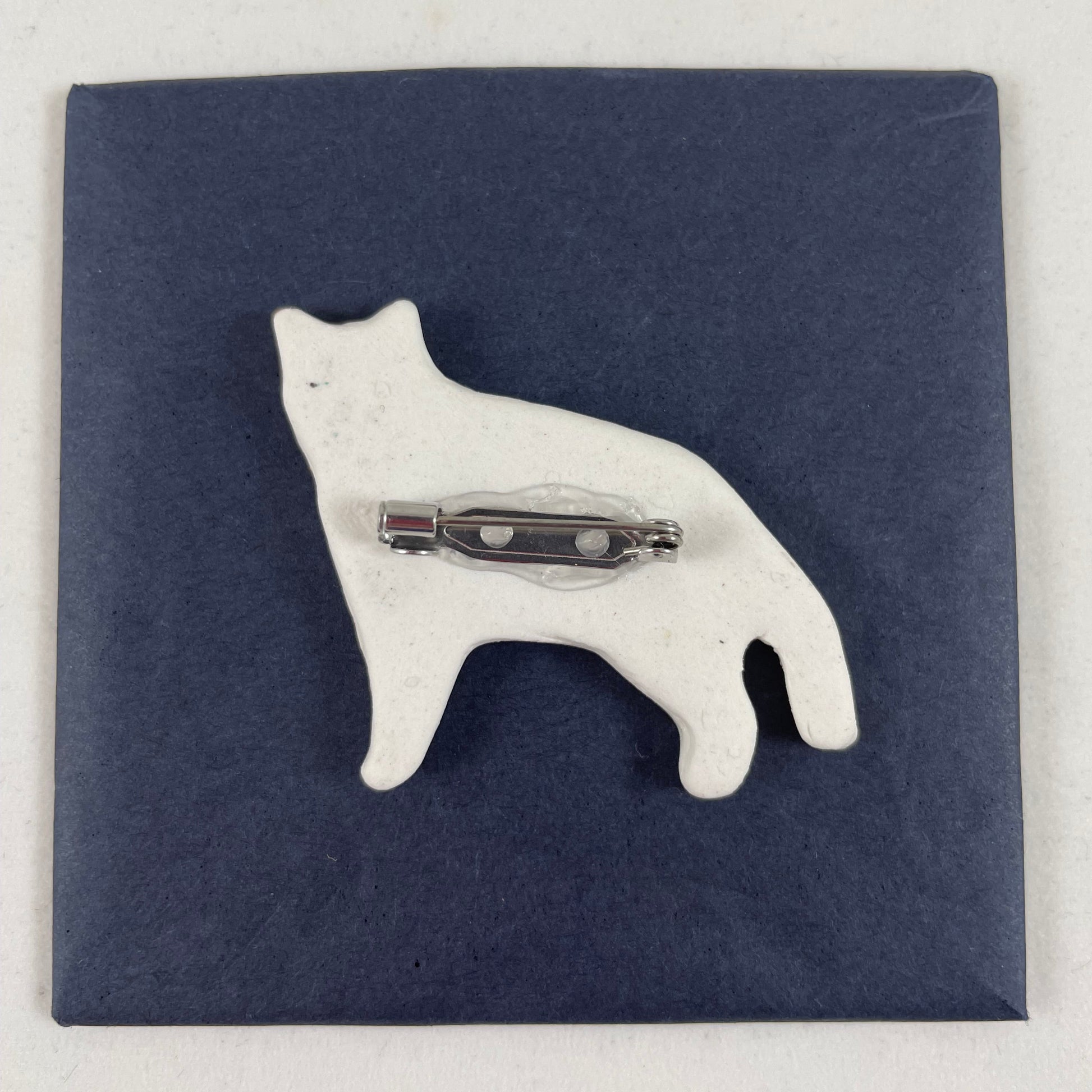 Back view of brooch. White unglazed porcelain with stainless steel brooch fastening glued on.