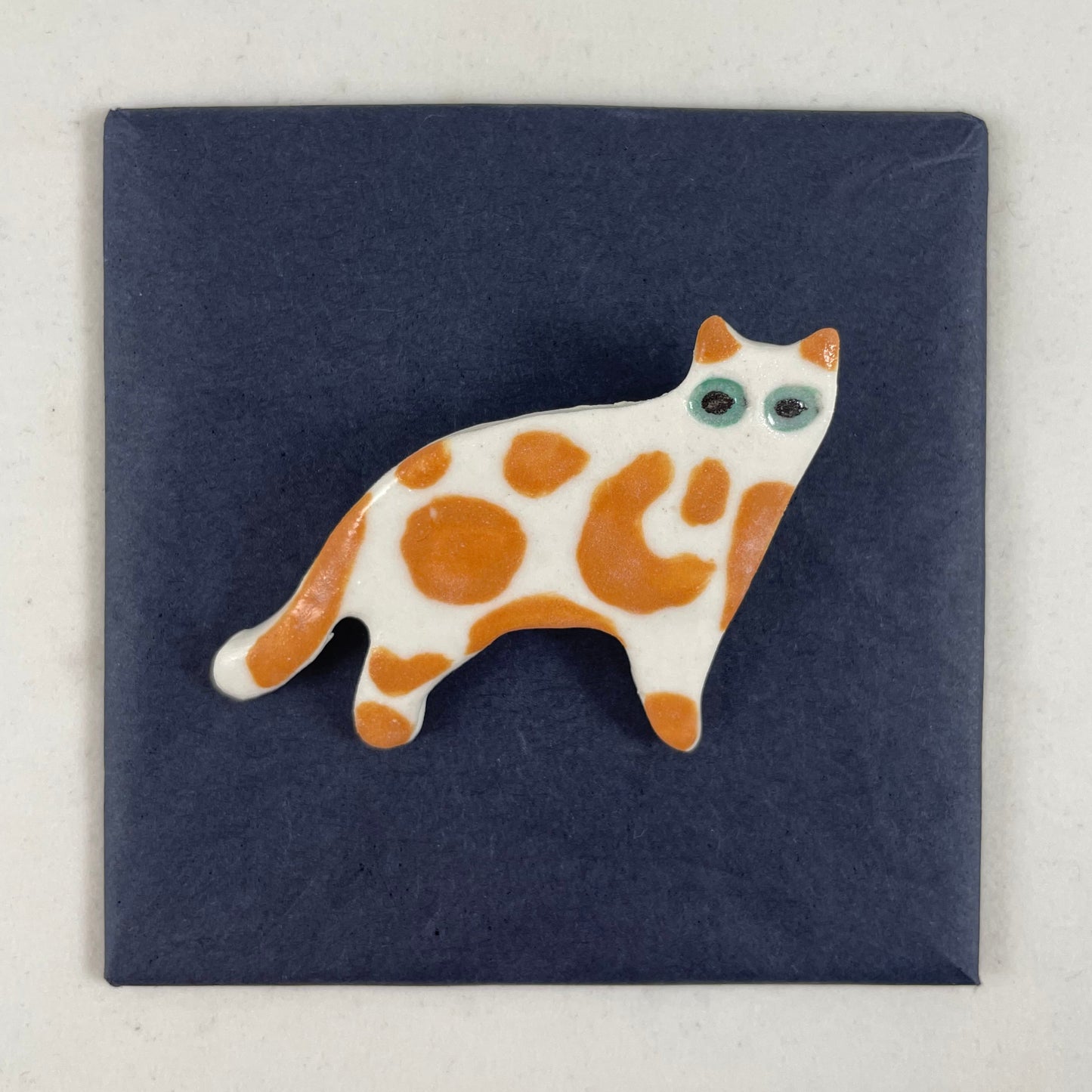 White porcelain cat with irregular orange spots and patches. Large green eyes. Photographed flat on a black background.