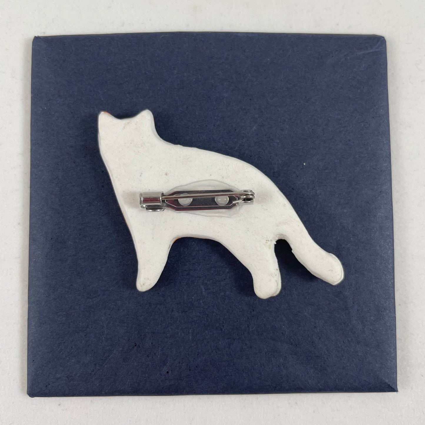Back view of brooch. White unglazed porcelain with stainless steel brooch fastening glued on.
