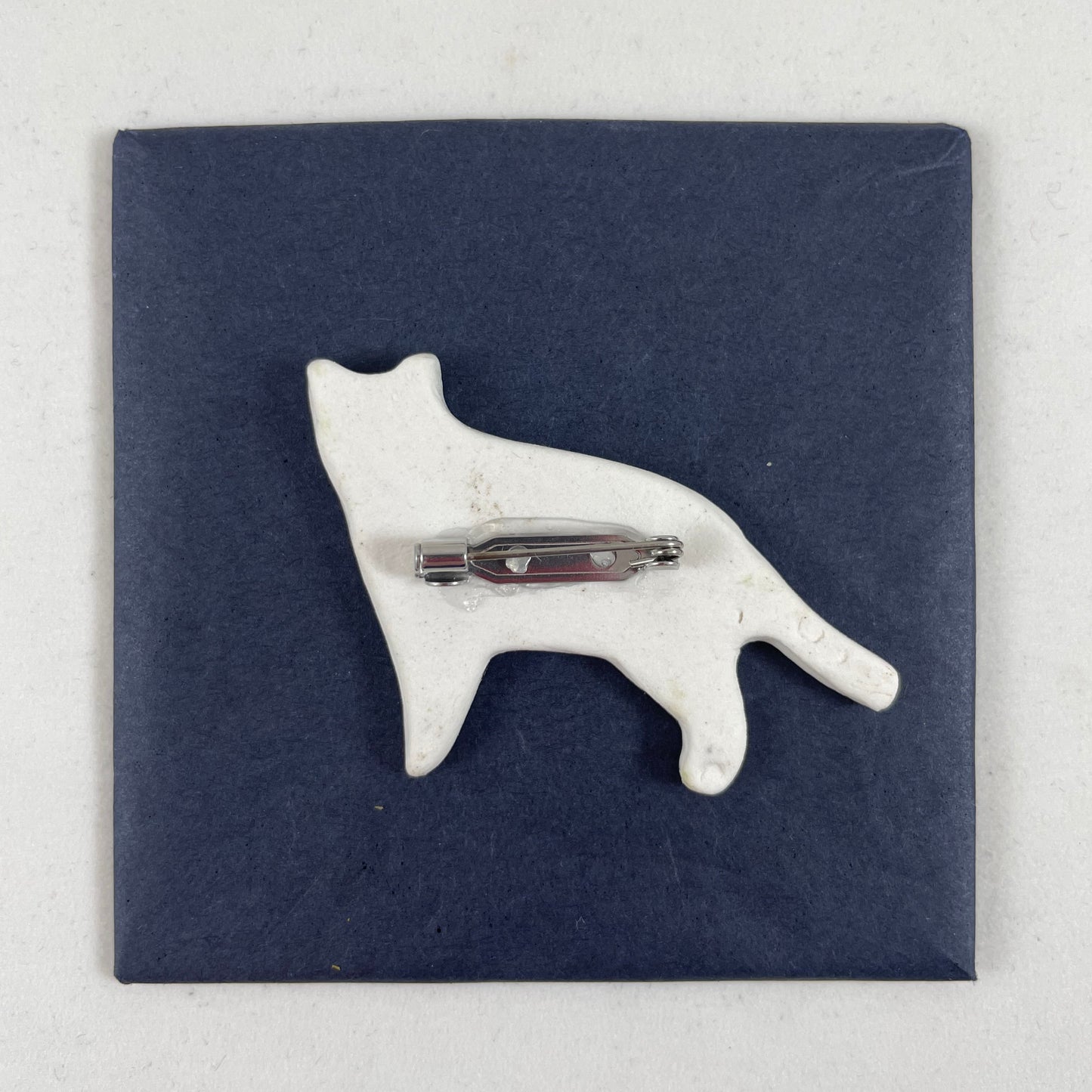 Back view of brooch. White unglazed porcelain with stainless steel brooch fastening glued on.