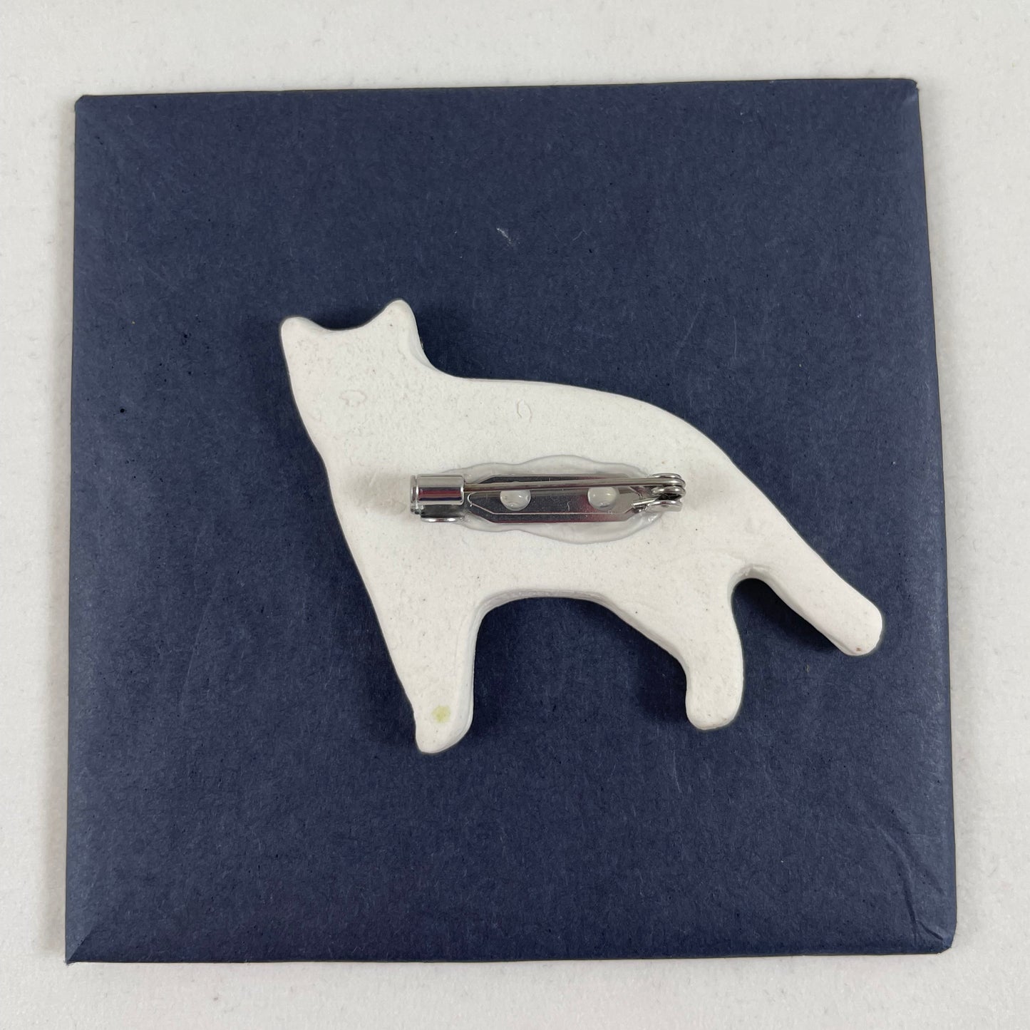 Back view of brooch. White unglazed porcelain with stainless steel brooch fastening glued on.