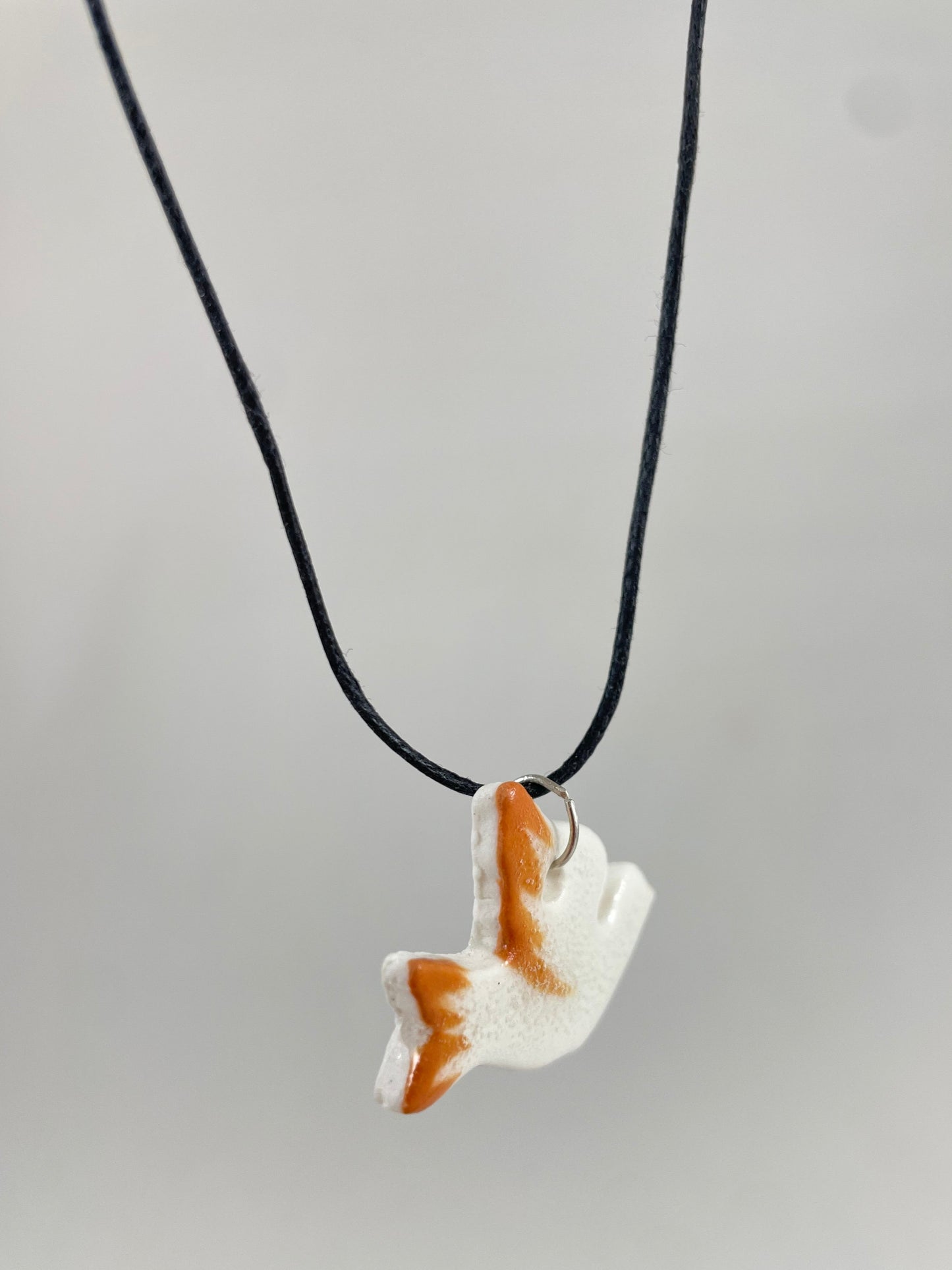 Necklace hanging against white background. Fine black thread with dove shaped pendant in white with orange wing and tail. Pendant is attached with small sterling silver jump ring. Side view taken from left hand side. Porcelain pendant is thin.