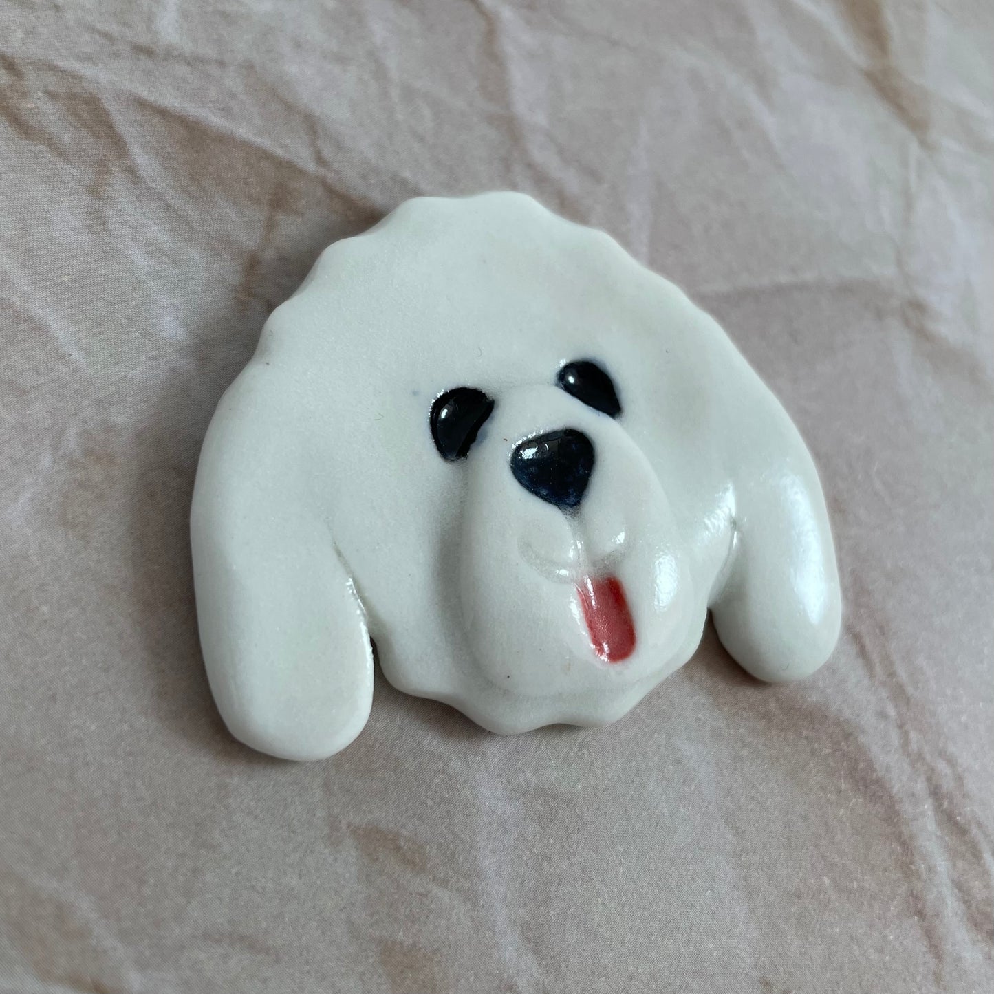 Dog's head in glossy white porcelain with long ears and rosy pink tongue sticking out. Shiny black eyes and nose. Muzzle area is slightly raised to stand out. Photographed from left hand side. Porcelain is thin