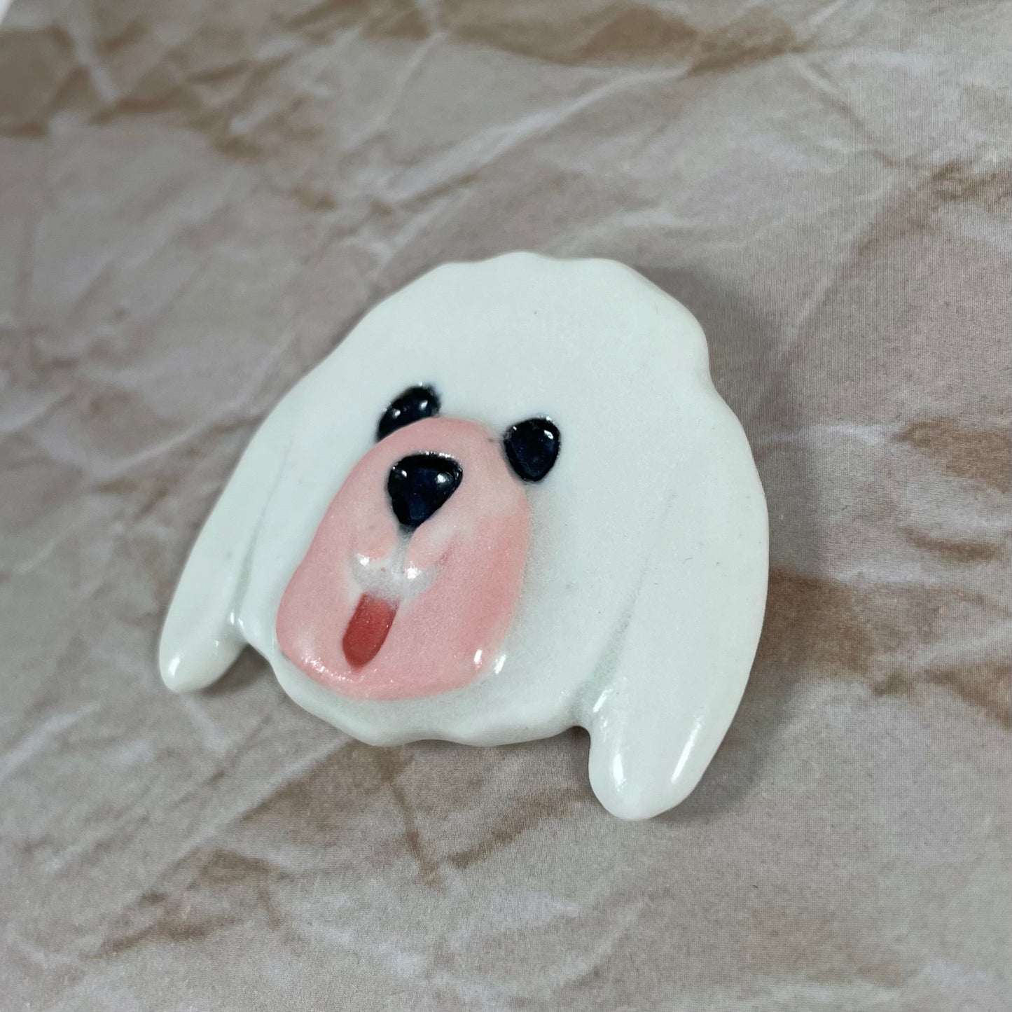 Dog's head in glossy white porcelain with long ears and rosy pink tongue sticking out. Shiny black eyes and nose. Muzzle area is pale pink and slightly raised to stand out. Photographed from right hand side. Porcelain is thin