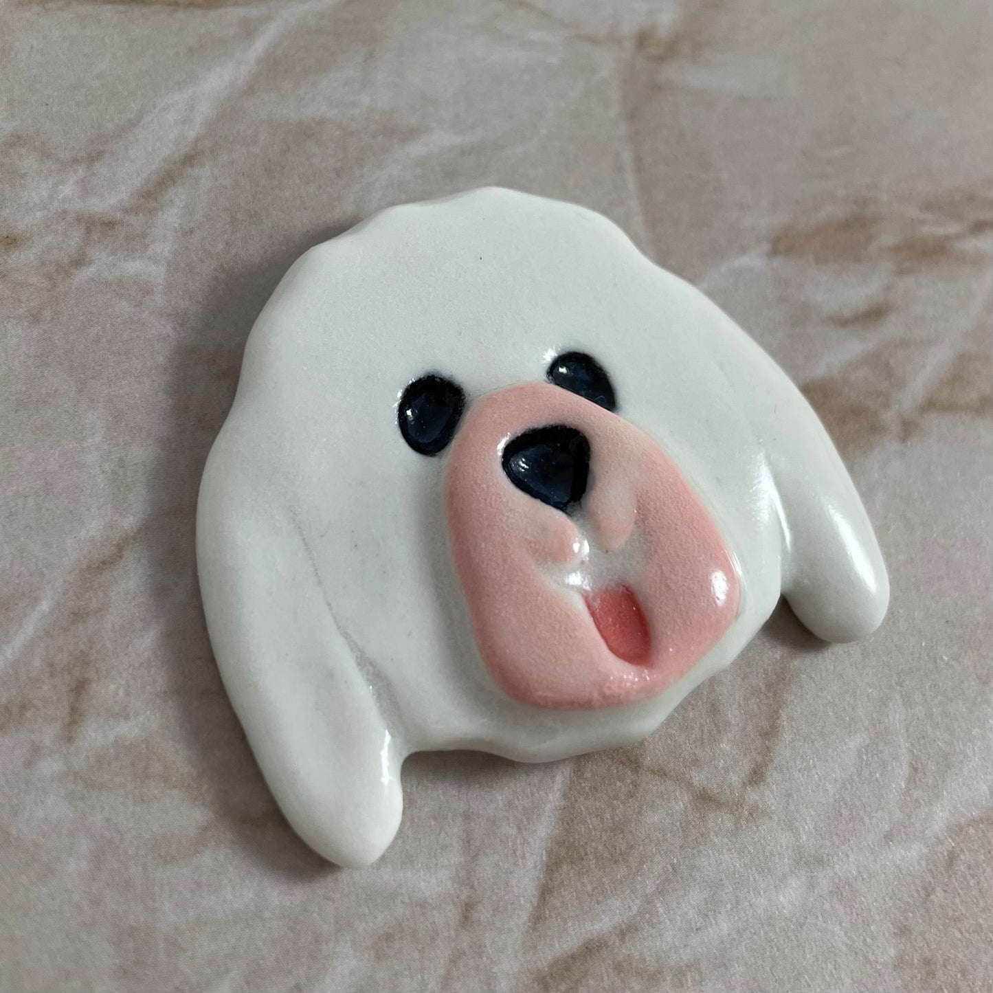 Dog's head in glossy white porcelain with long ears and rosy pink tongue sticking out. Shiny black eyes and nose. Muzzle area is pale pink and slightly raised to stand out. Photographed from left hand side. Porcelain is thin