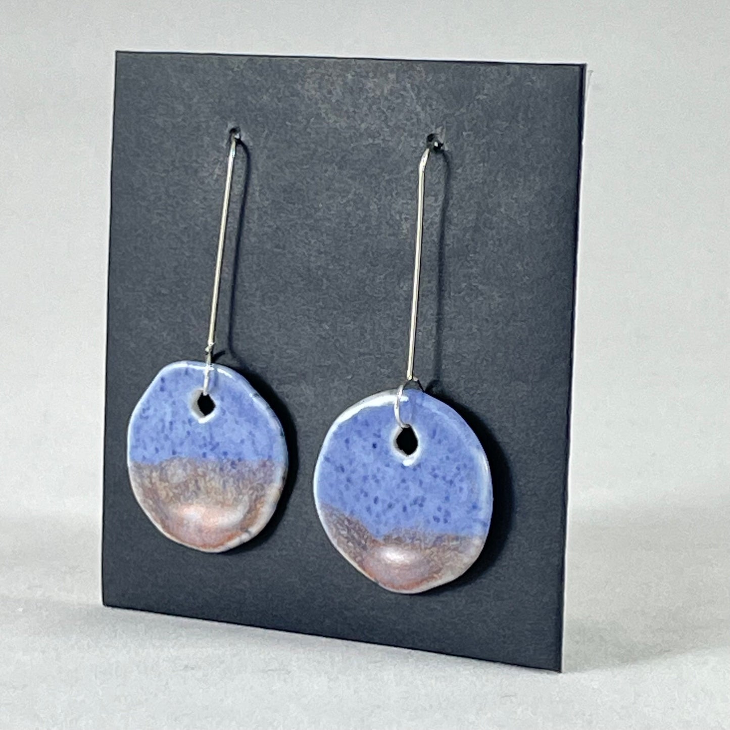 A pair of hand formed porcelain earrings in blue with mauve and orange flecks. Side view showing thin earring profile