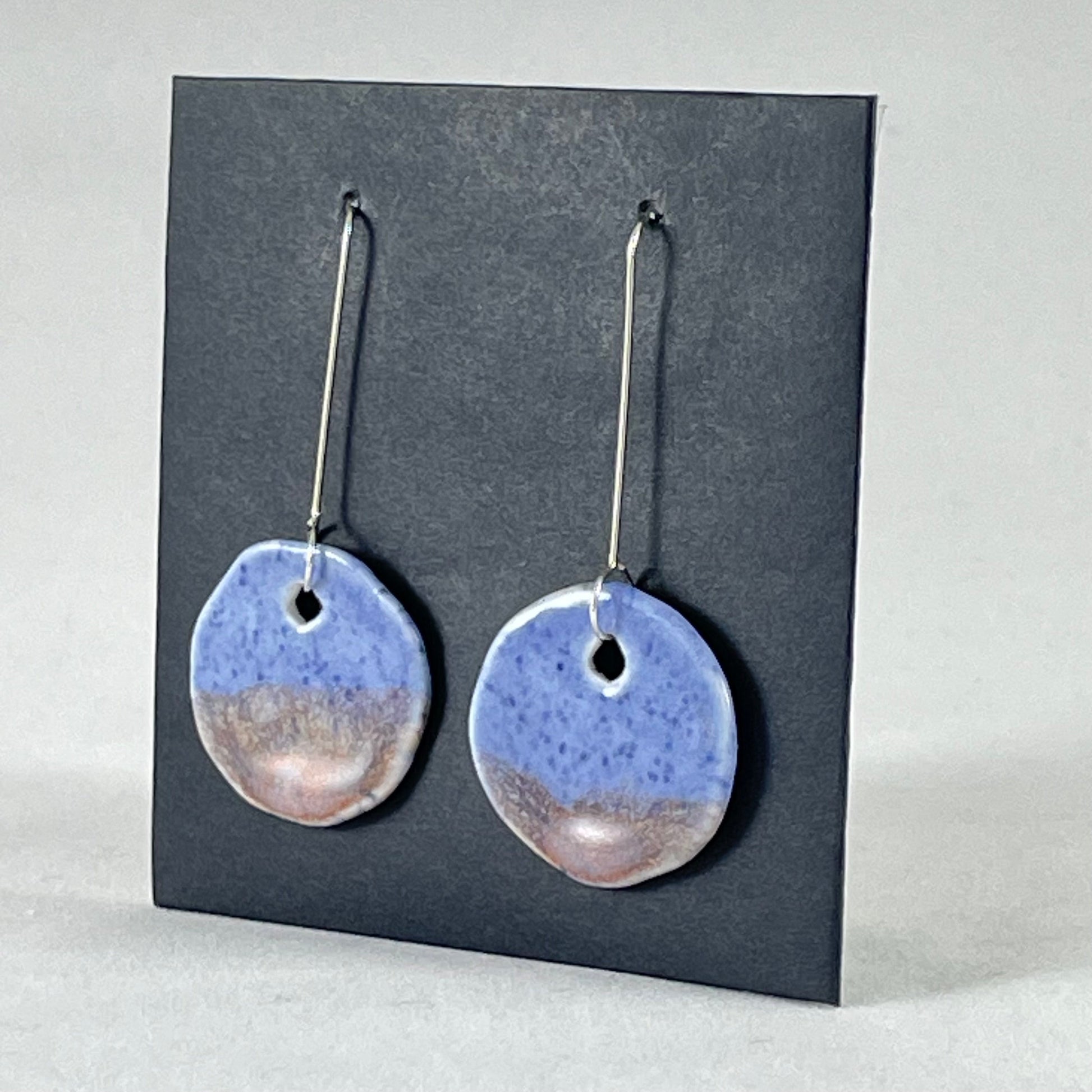 A pair of hand formed porcelain earrings in blue with mauve and orange flecks. Side view showing thin earring profile