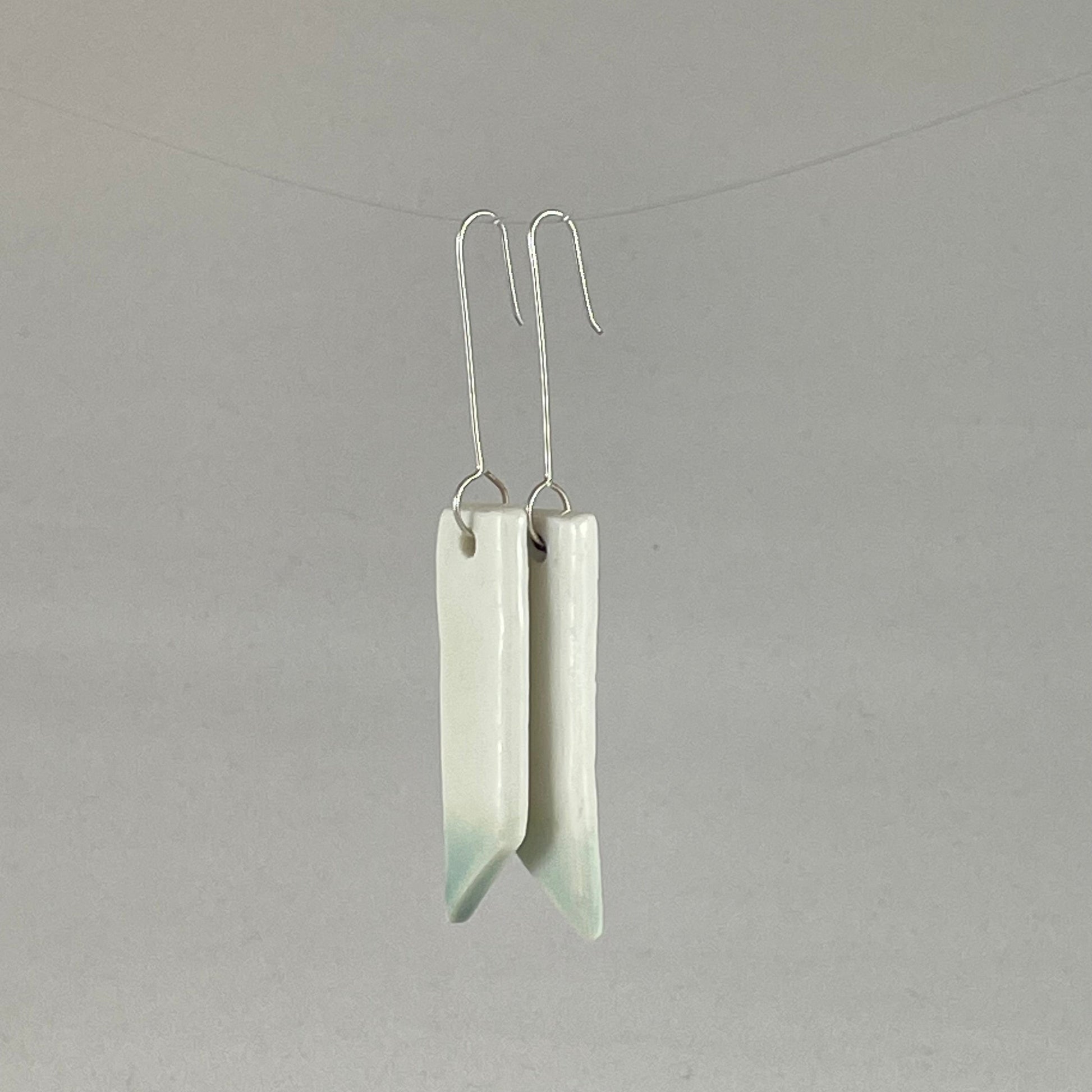 A pair of hand formed porcelain pendant earrings in glossy white and a hint of mint green. Side view showing thin earring profile