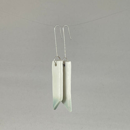 A pair of hand formed porcelain pendant earrings in glossy white and a hint of mint green. Side view showing thin earring profile