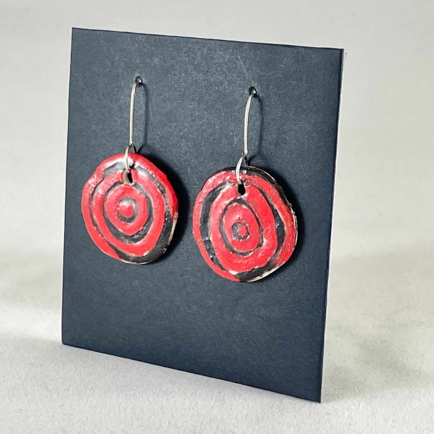 A pair of hand formed porcelain pendant earrings in striking black and red abstract flower pattern. Side view showing thin earring profile