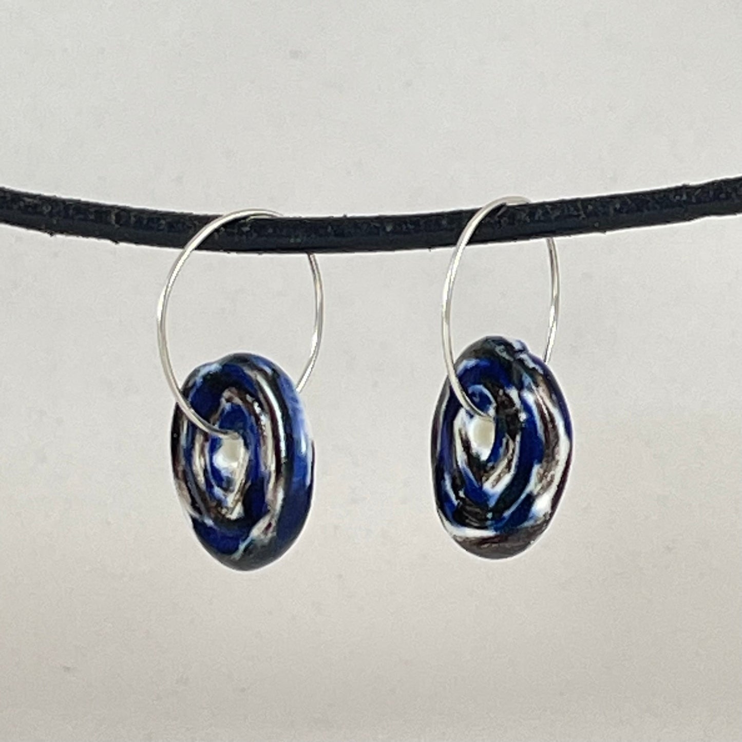A pair of silver hoops with hand formed porcelain pendants in blue black and white. Side view showing thin earring profile