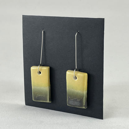 Pair of hand formed porcelain pendant earrings. Yellow and warm green bands of colour on rectangle shape. Sterling silver hooks. Side view