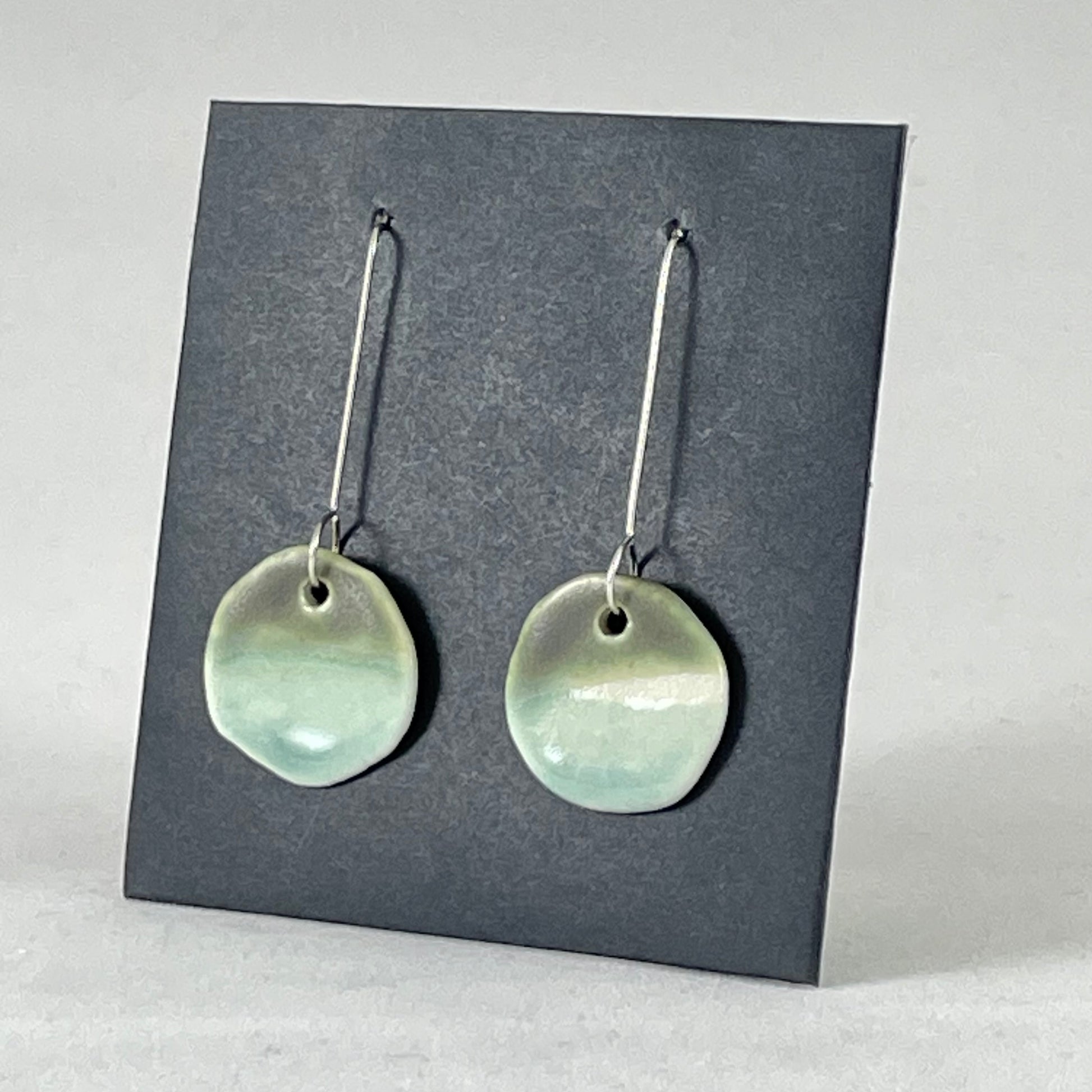 Pair of circular mint and green porcelain earrings. On long sterling silver earring hooks. Side view