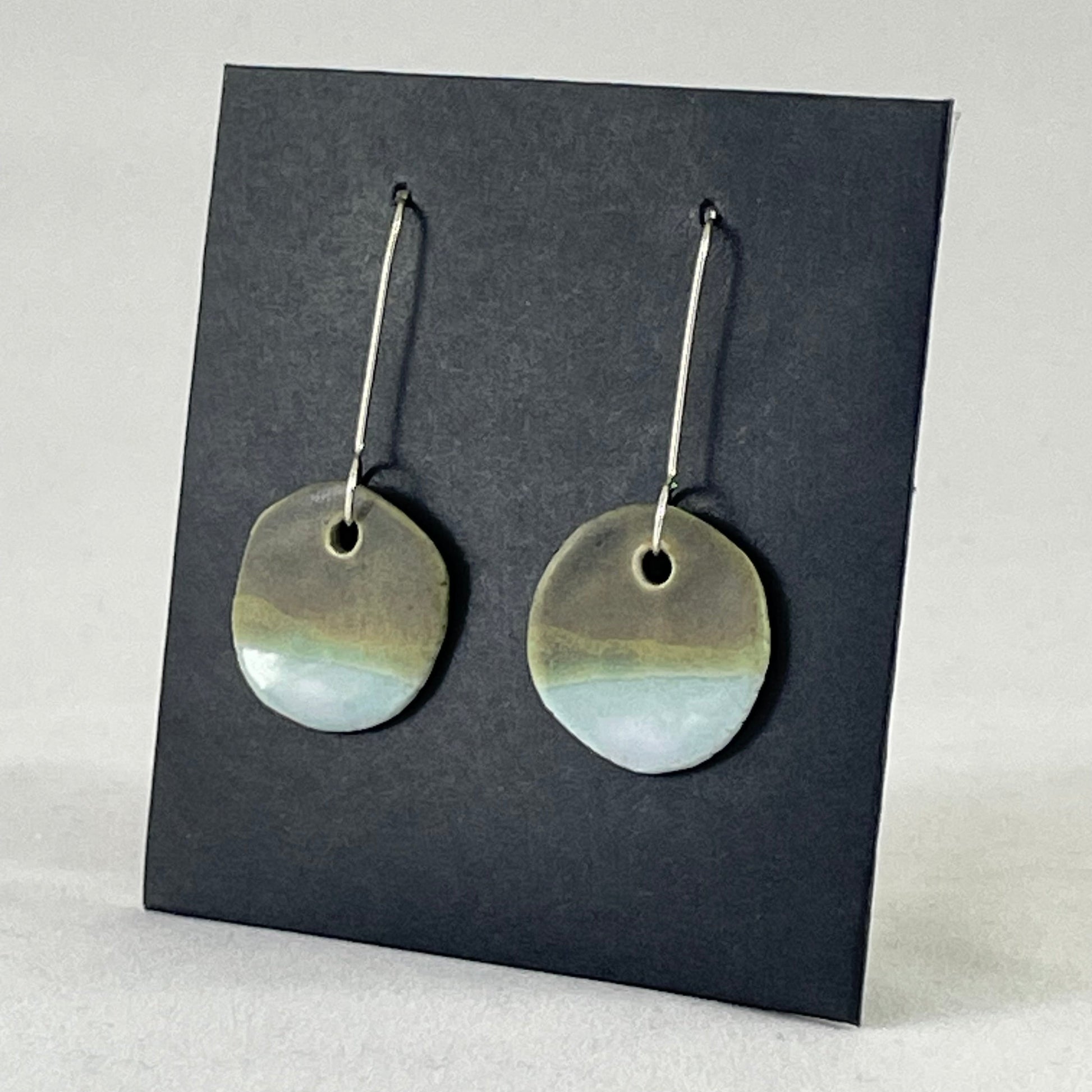 A pair of circular porcelain earrings in blue and green. On sterling silver earrings hooks. Side view