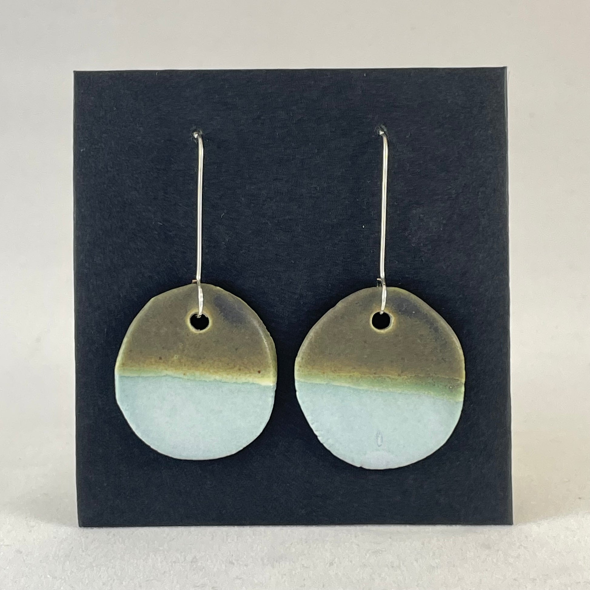 A pair of circular porcelain earrings in blue and green. On sterling silver earrings hooks.