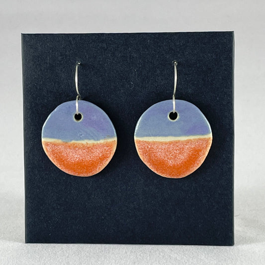A pair of circular shaped porcelain earrings in purple and orange. On sterling silver earrings hooks.