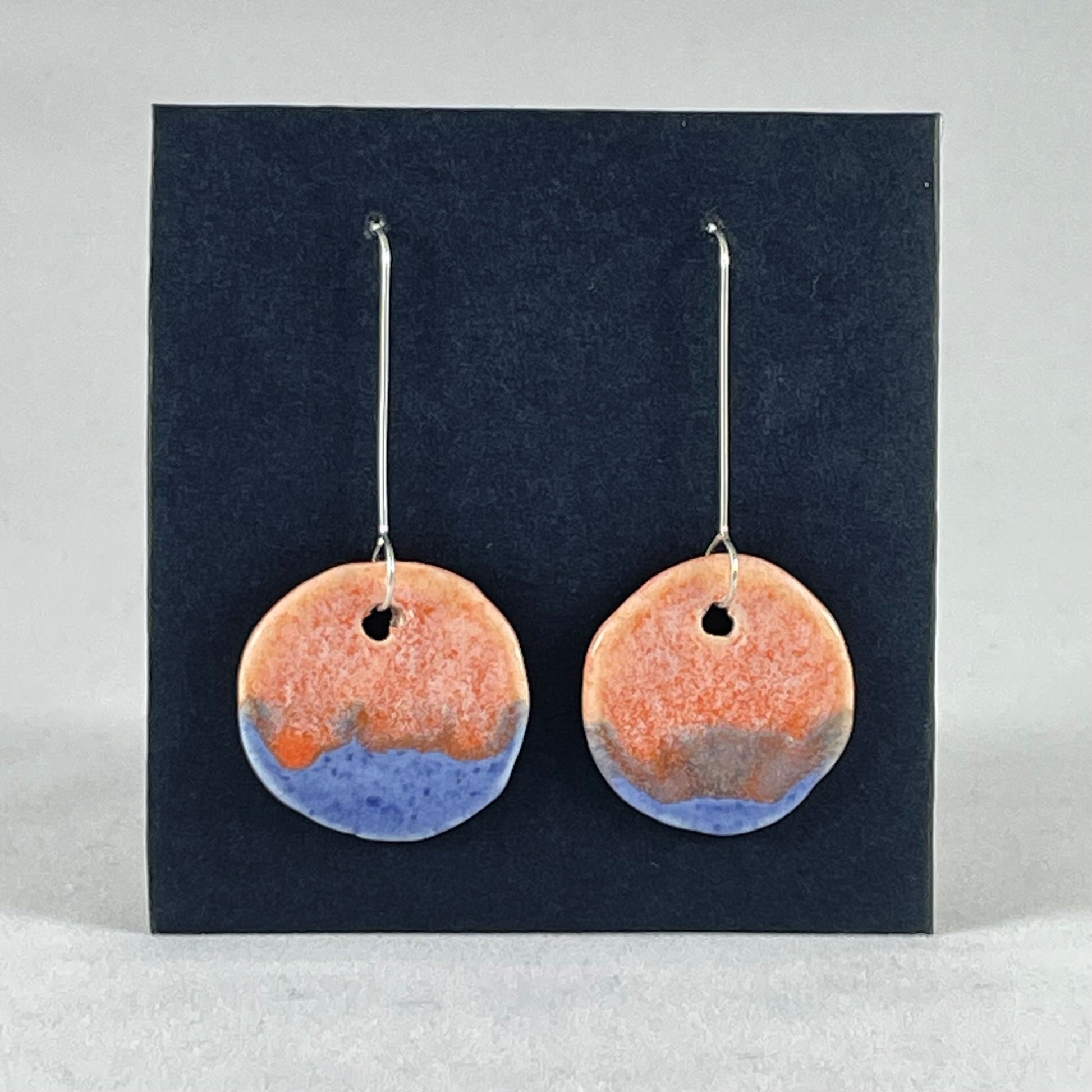 A pair of circular shaped porcelain earrings in blue and orange. On sterling silver earrings hooks. 