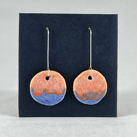 A pair of circular shaped porcelain earrings in blue and orange. On sterling silver earrings hooks. 