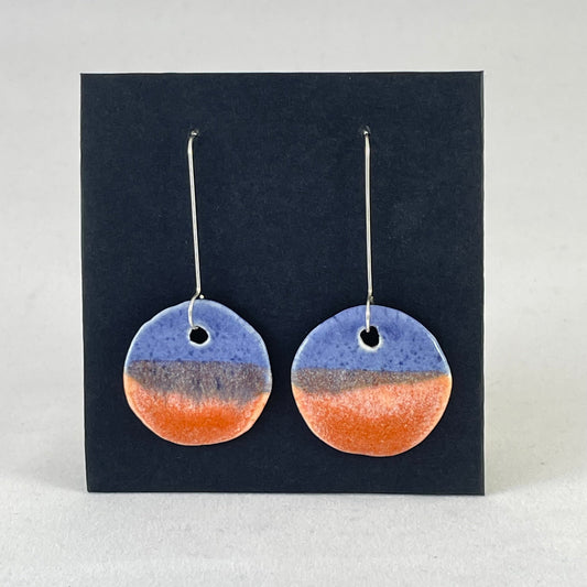 A pair of circular shaped porcelain earrings in blue and orange. On sterling silver earrings hooks. 