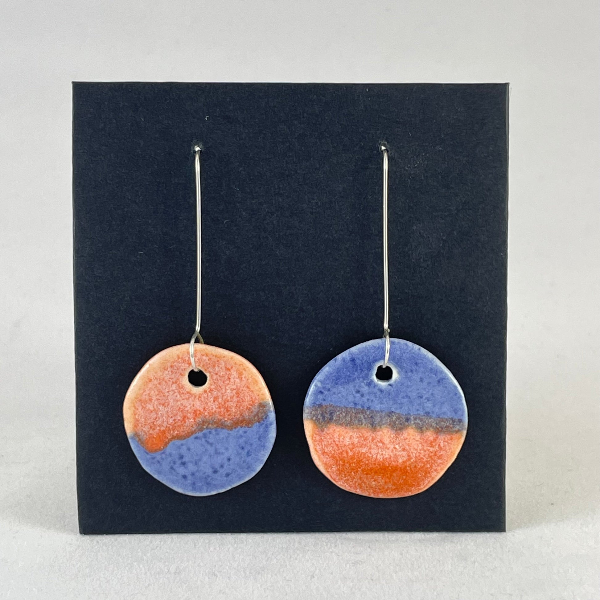 A pair of circular shaped porcelain earrings in blue and orange. On sterling silver earrings hooks. 