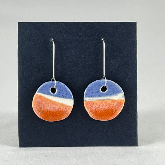A pair of circular shaped porcelain earrings in blue white and orange. On sterling silver earrings hooks. 