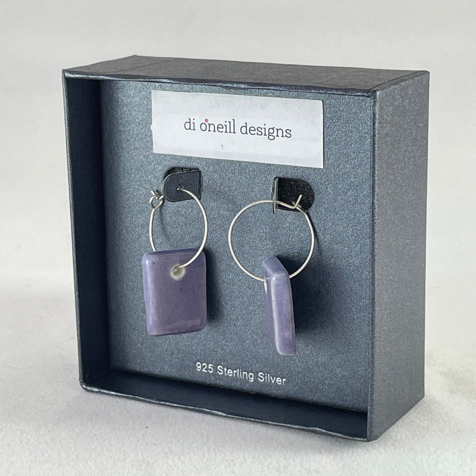 Side view of a pair of rectangular shaped porcelain hoop earrings in purple. On sterling silver earrings hooks.