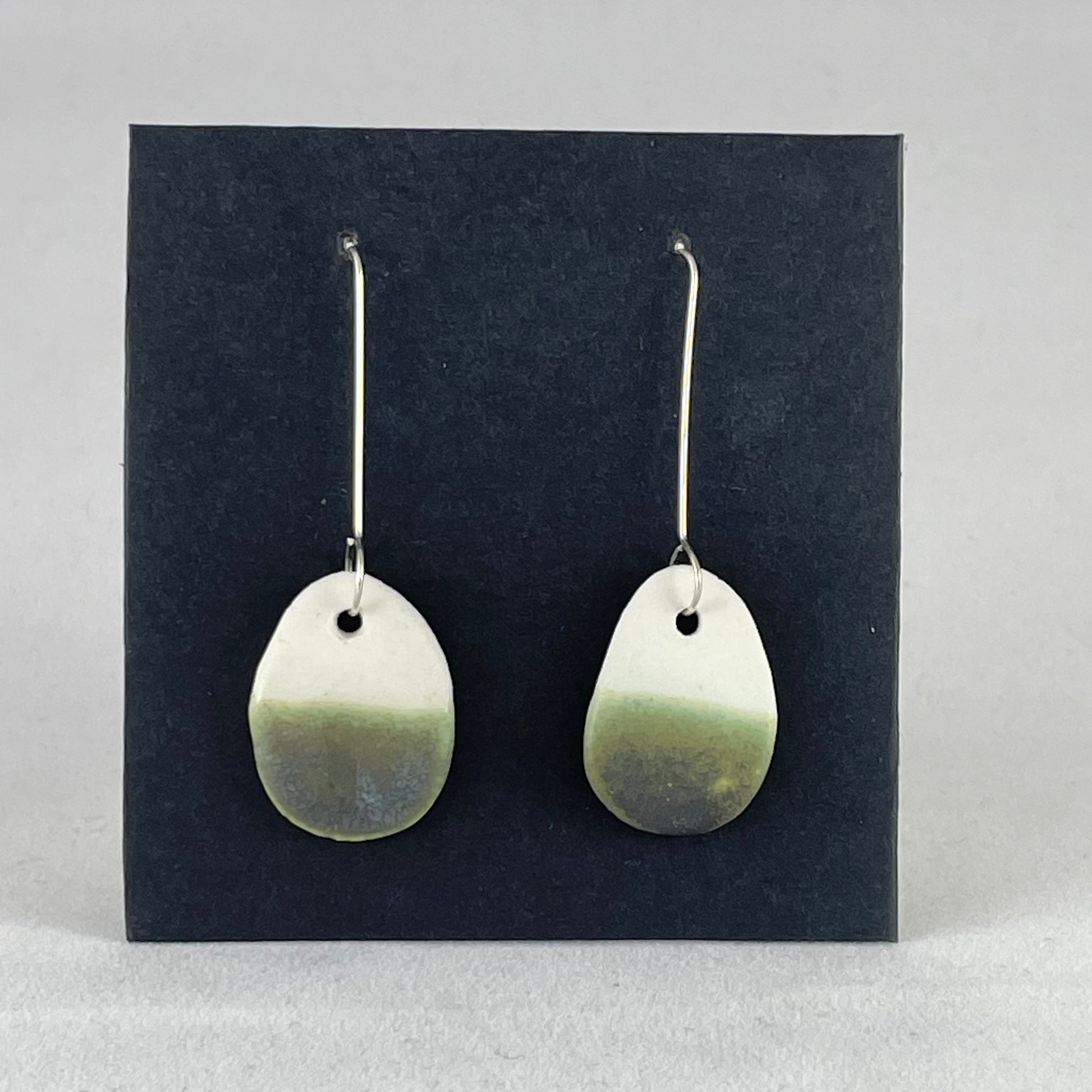 A pair of oval shaped porcelain earrings in white and green. On sterling silver earrings hooks.