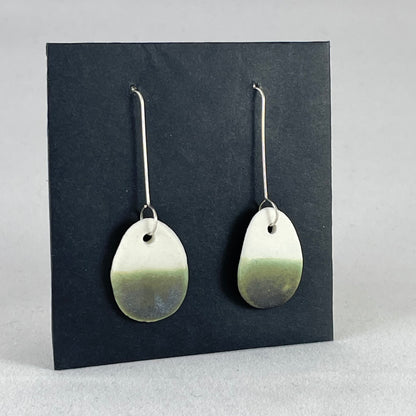 Side view of a pair of oval shaped porcelain earrings in dark green and white. On sterling silver earrings hooks.