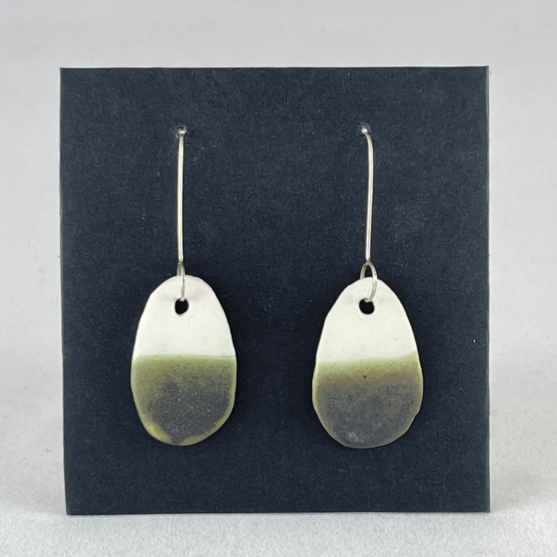 A pair of oval shaped porcelain earrings in white and green. On sterling silver earrings hooks.