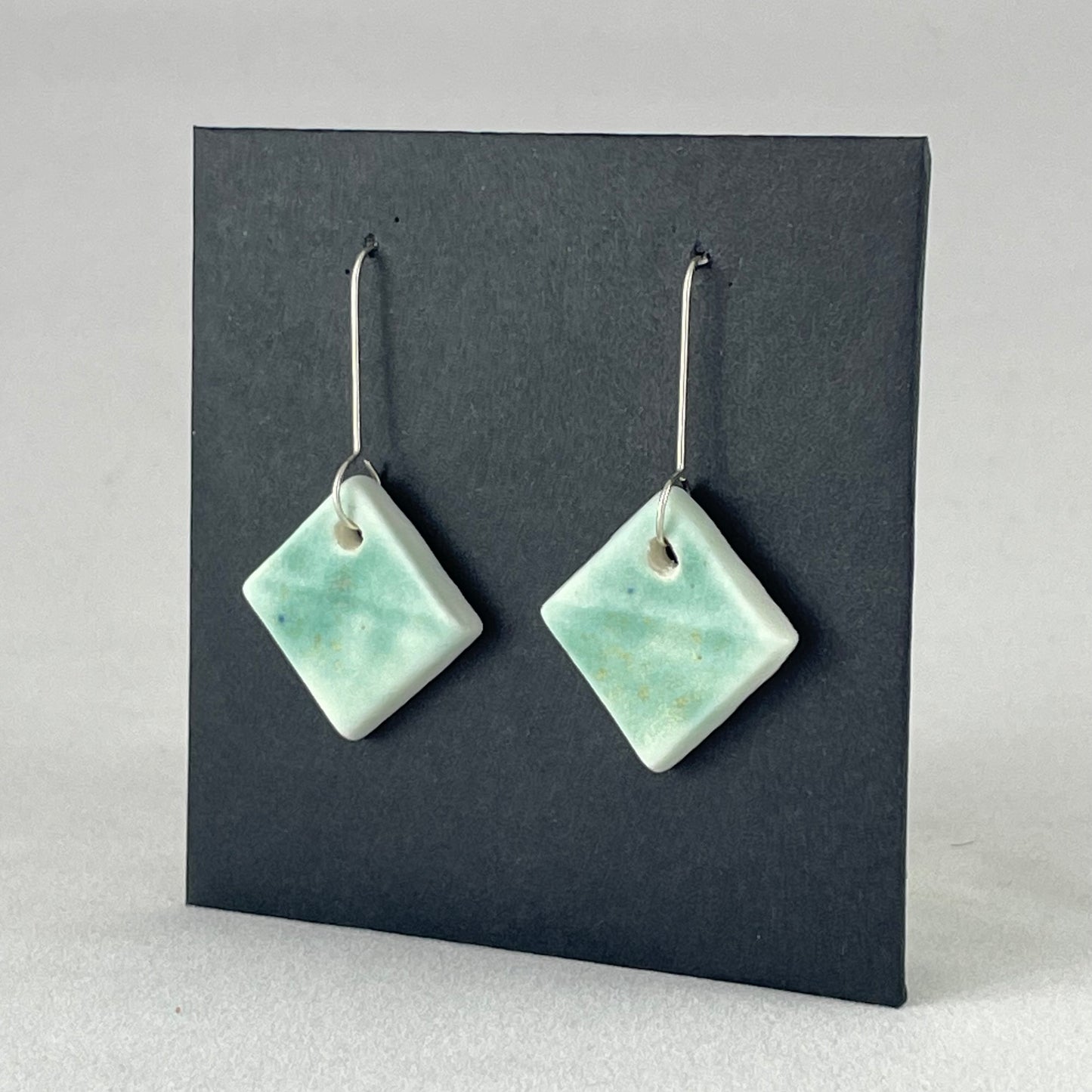 A pair of diamond shaped porcelain earrings in green. On sterling silver earrings hooks. Side view