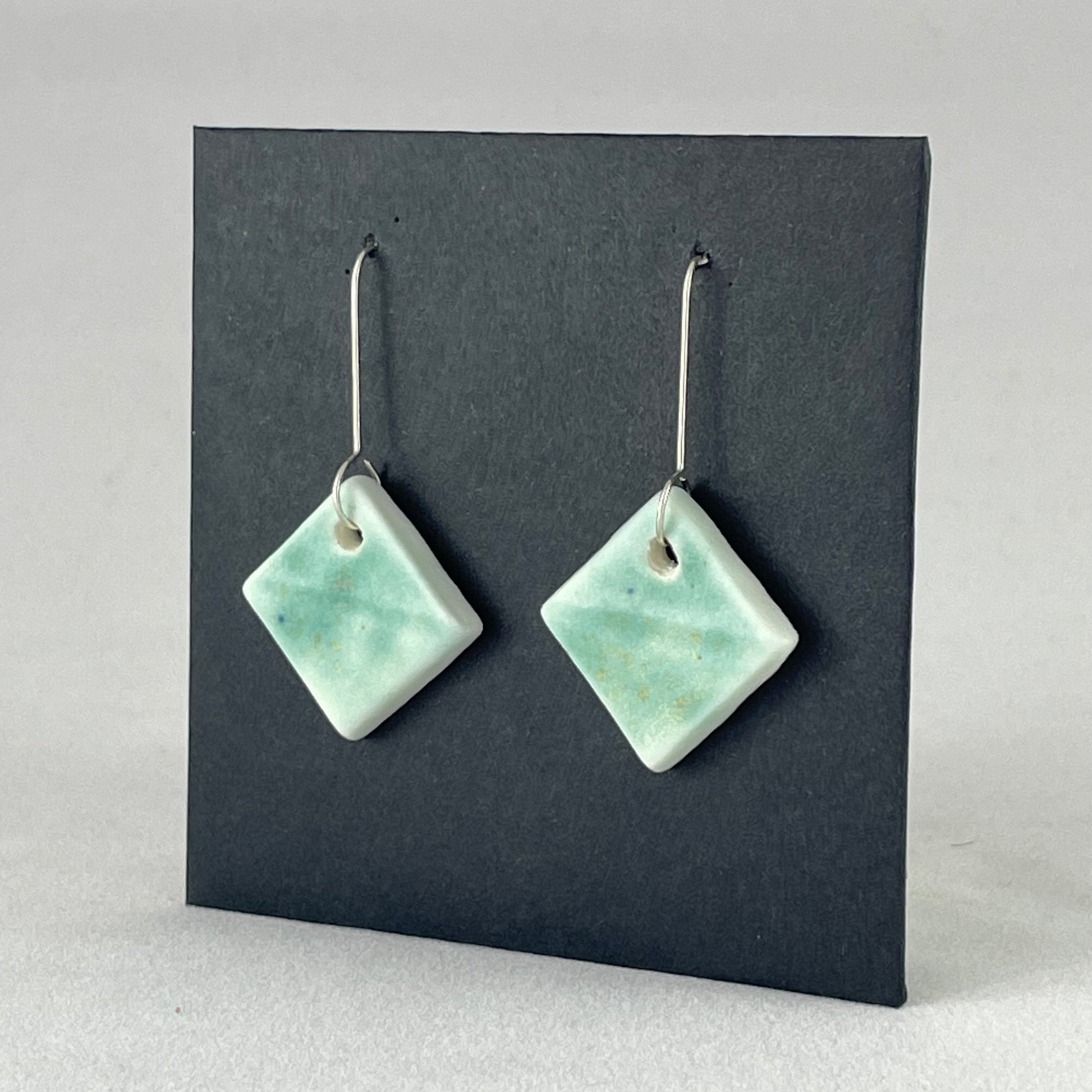 A pair of diamond shaped porcelain earrings in green. On sterling silver earrings hooks. Side view